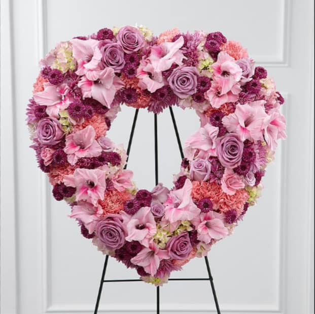 Heart-shaped floral wreath in pink and purple tones on a black stand