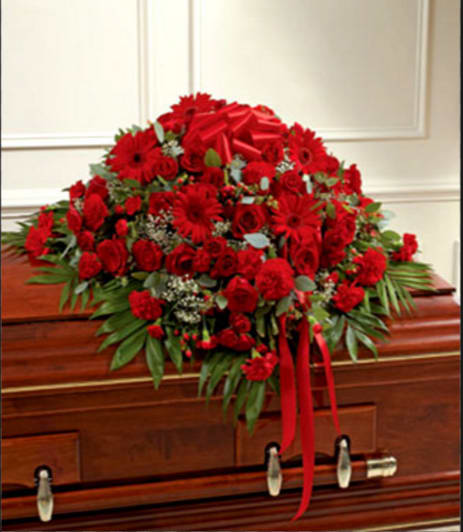 Red floral casket spray with ribbon on a wooden casket