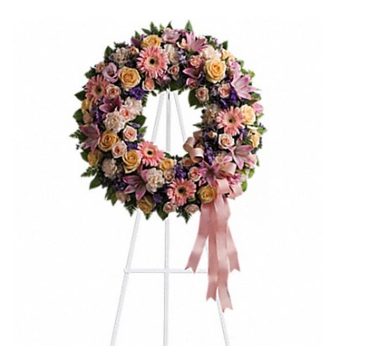 Circular floral wreath on a stand with pink and peach flowers and a ribbon