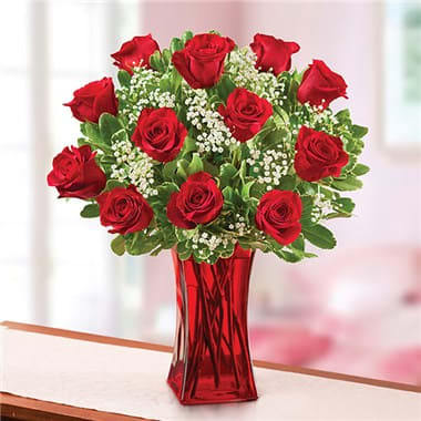 Red roses arranged in a red glass vase with white filler flowers
