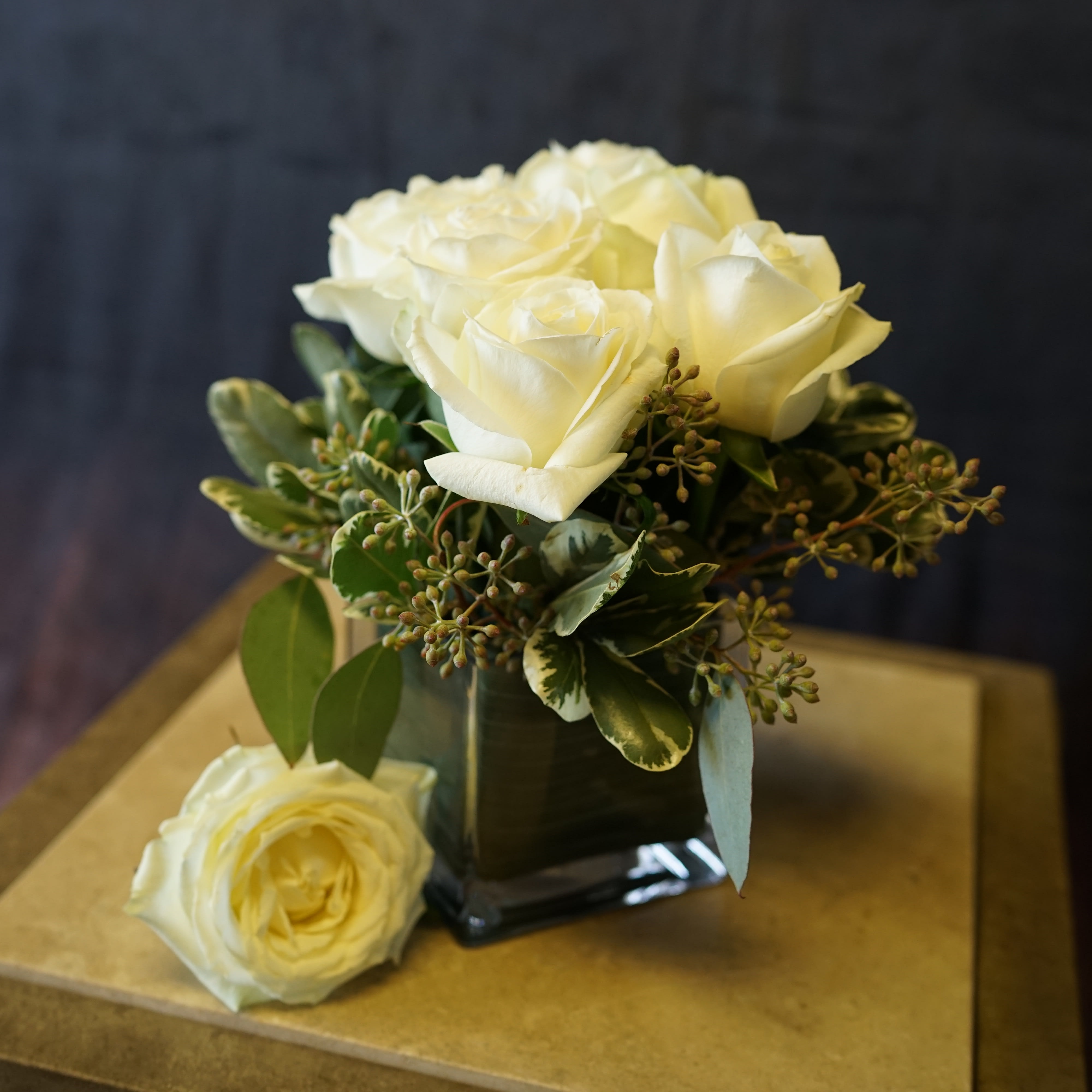 White roses arranged in a square glass vase with greenery