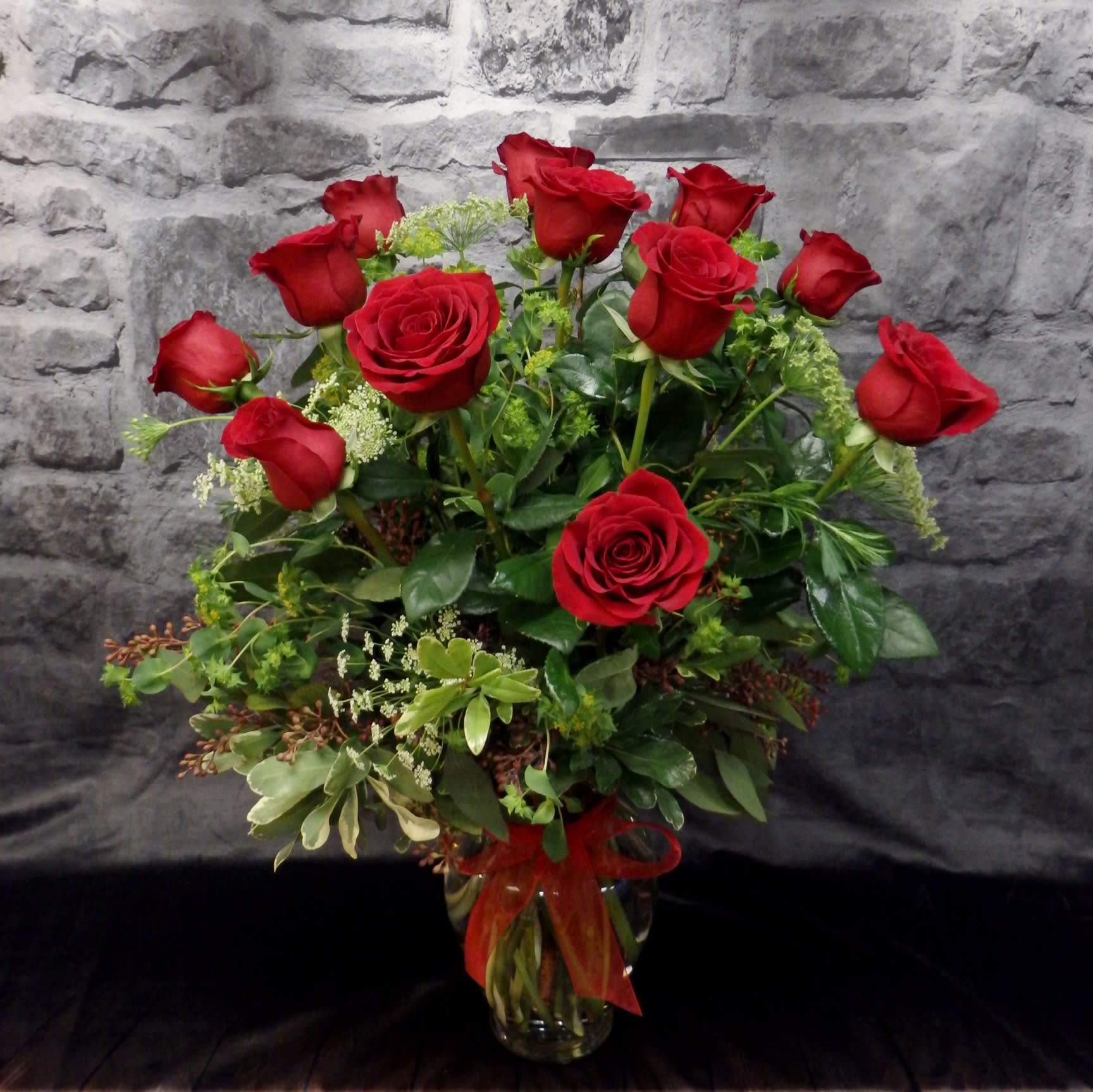 Red roses arranged in a clear glass vase with a red ribbon