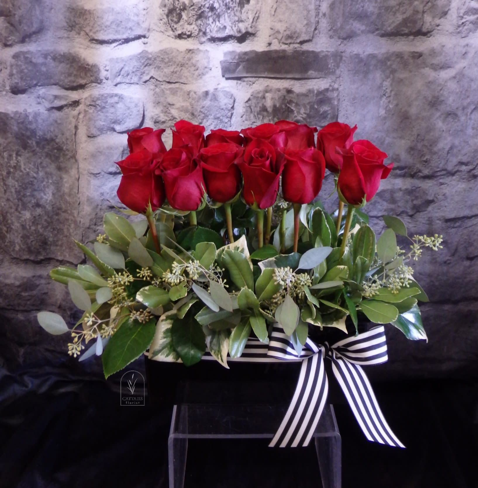 Red roses arranged in a black box with a striped ribbon
