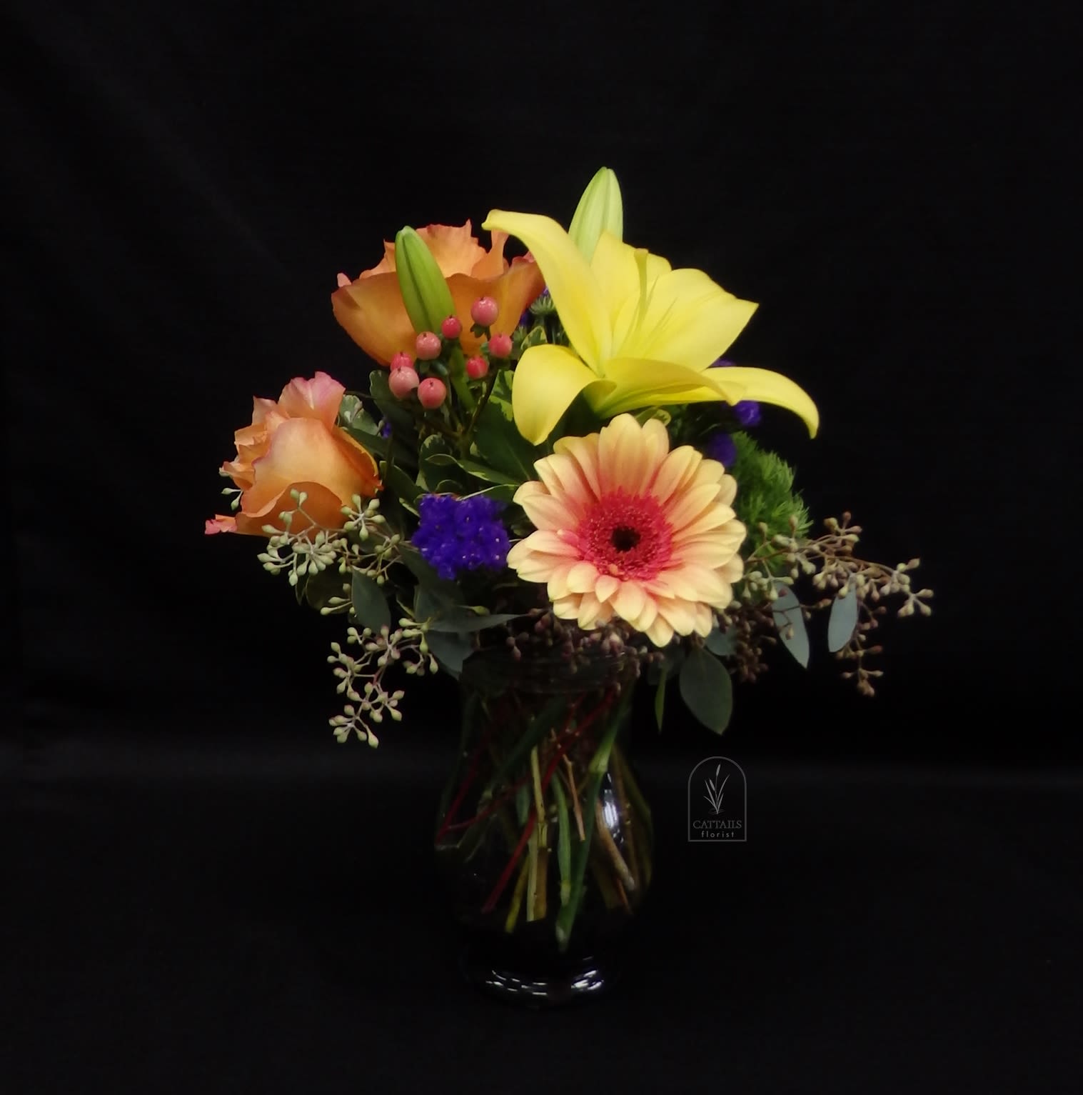 Mixed bouquet with yellow lily, peach roses, and a gerbera daisy in a glass vase