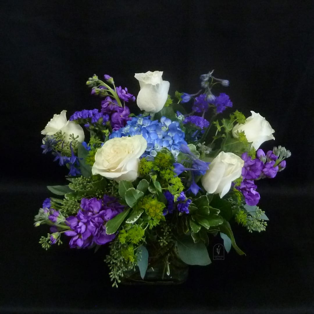 White roses and blue-purple flowers in a glass vase