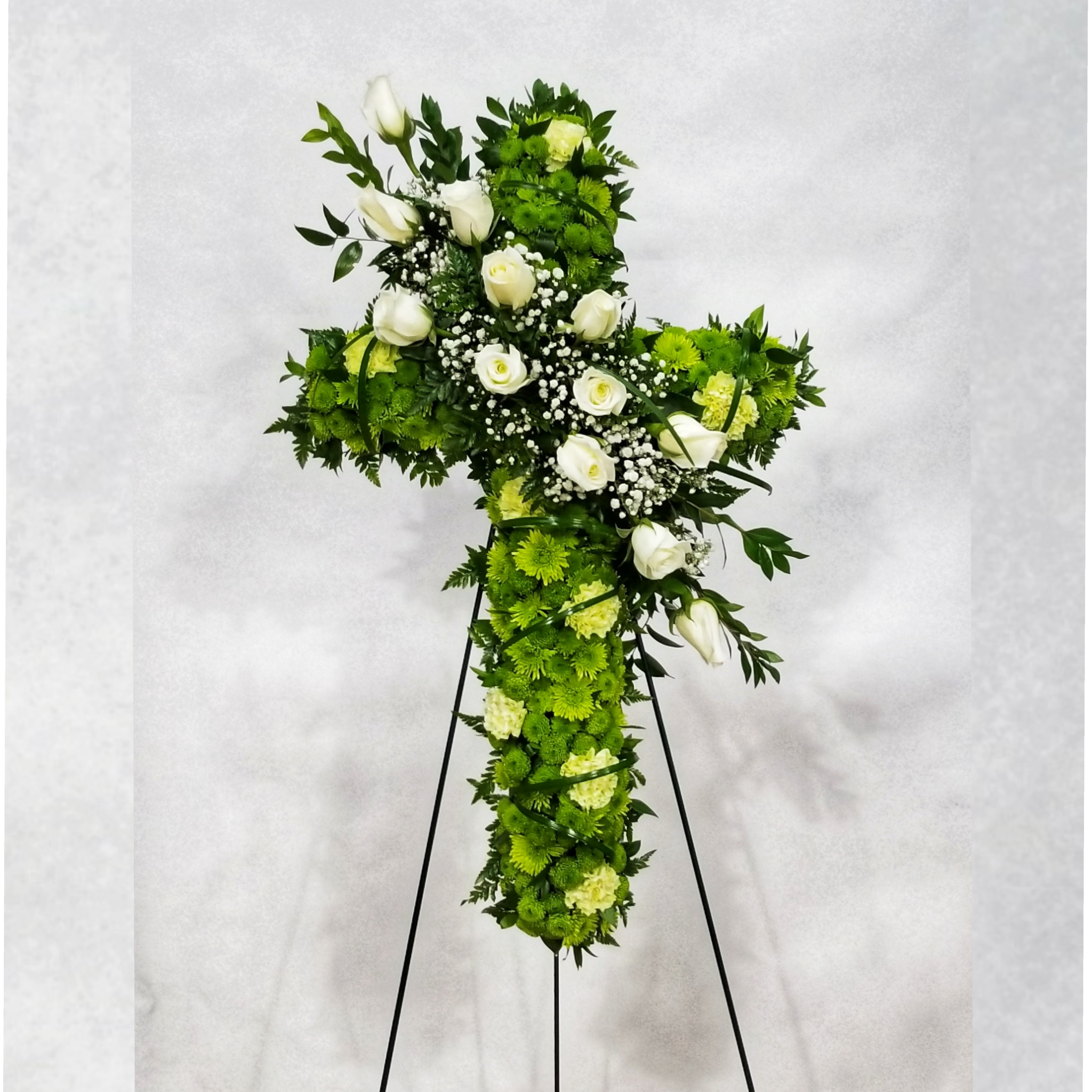 Cross-shaped floral tribute with white roses and green flowers on a stand