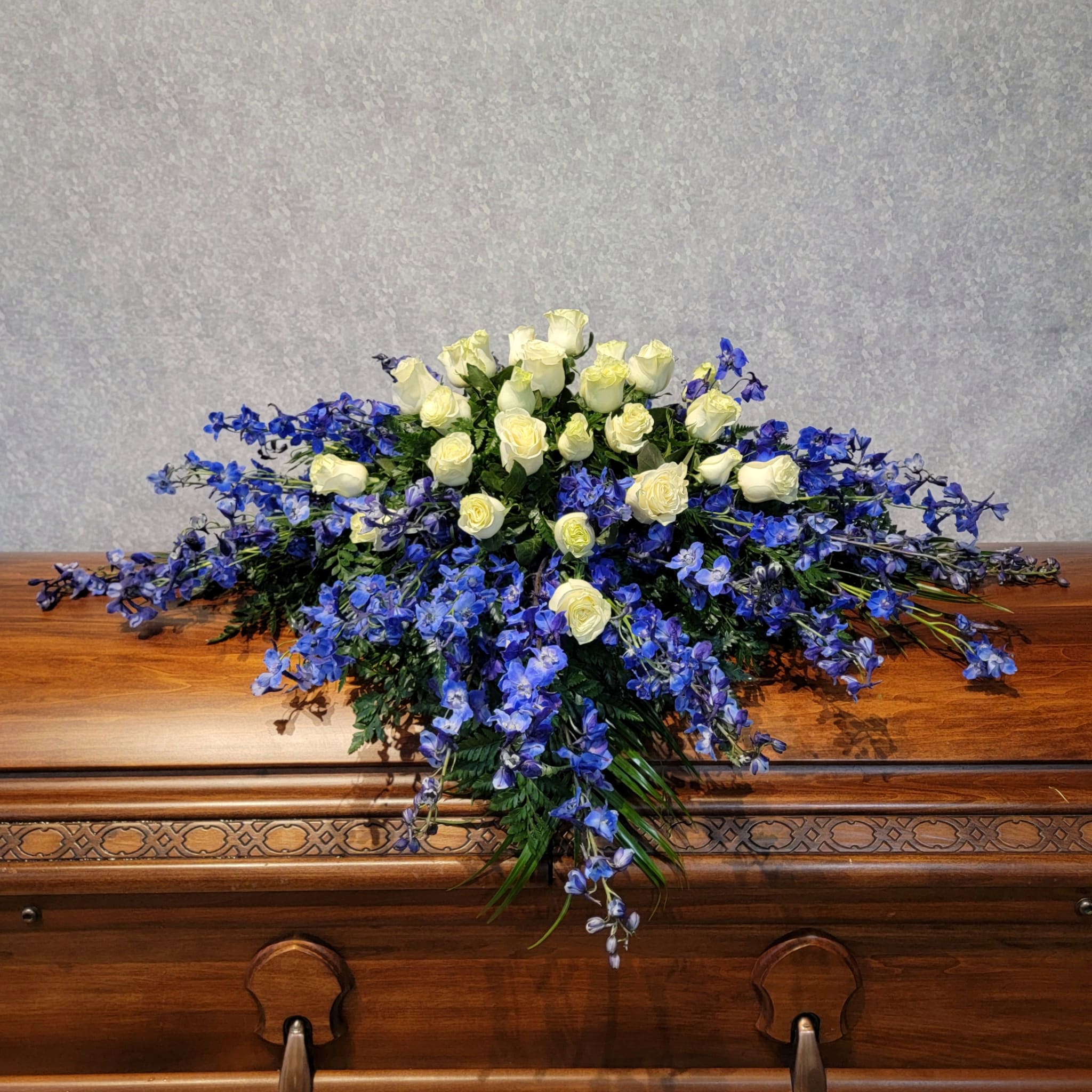 White roses and blue flowers arranged on a wooden casket