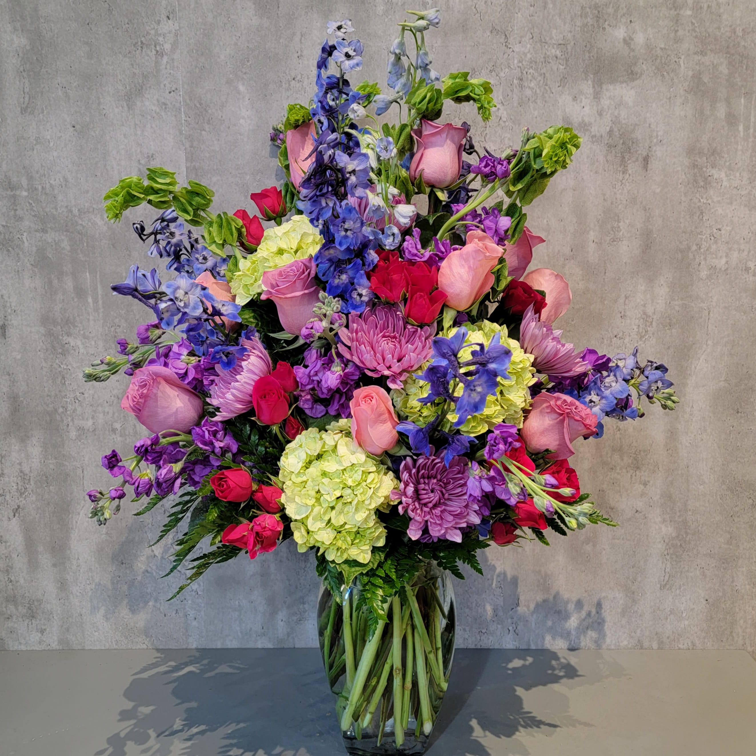 Large mixed bouquet of pink, purple, blue, and green flowers in a glass vase