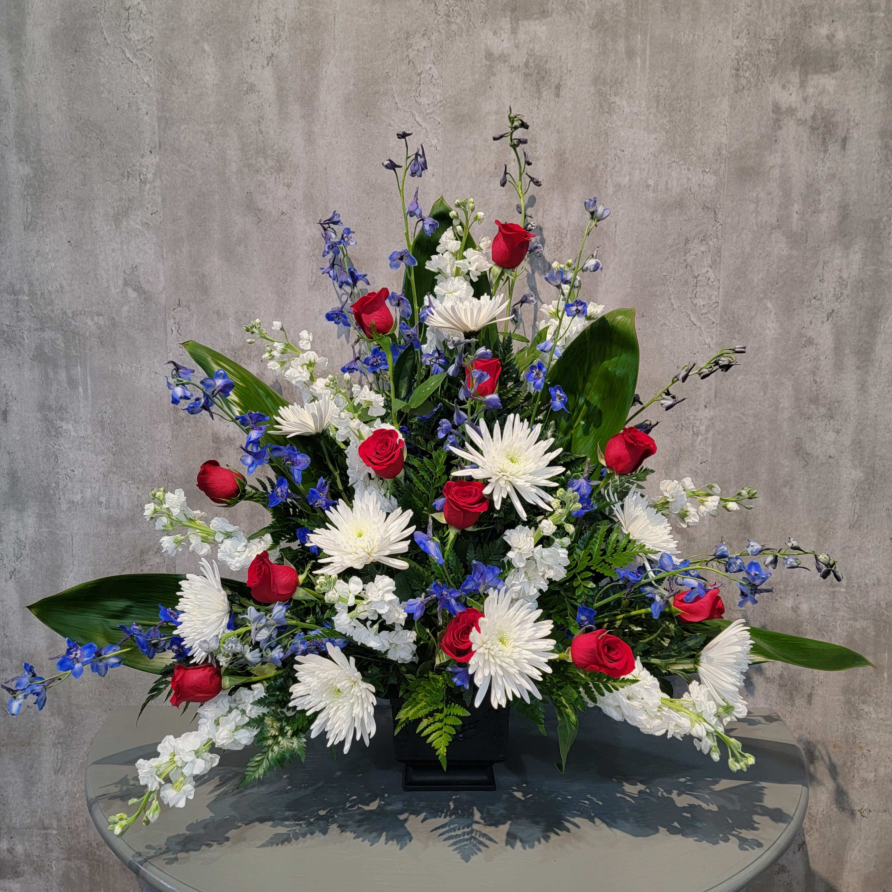 Red roses, white daisies, and blue flowers in a black vase
