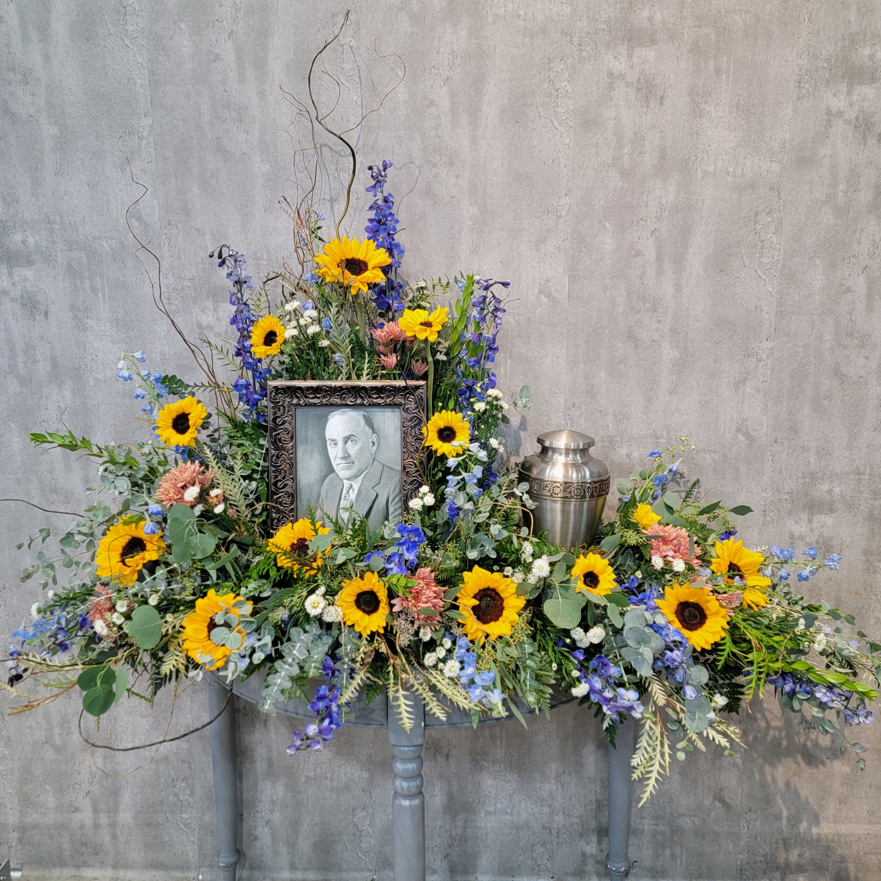 Large memorial floral arrangement with sunflowers and a framed portrait