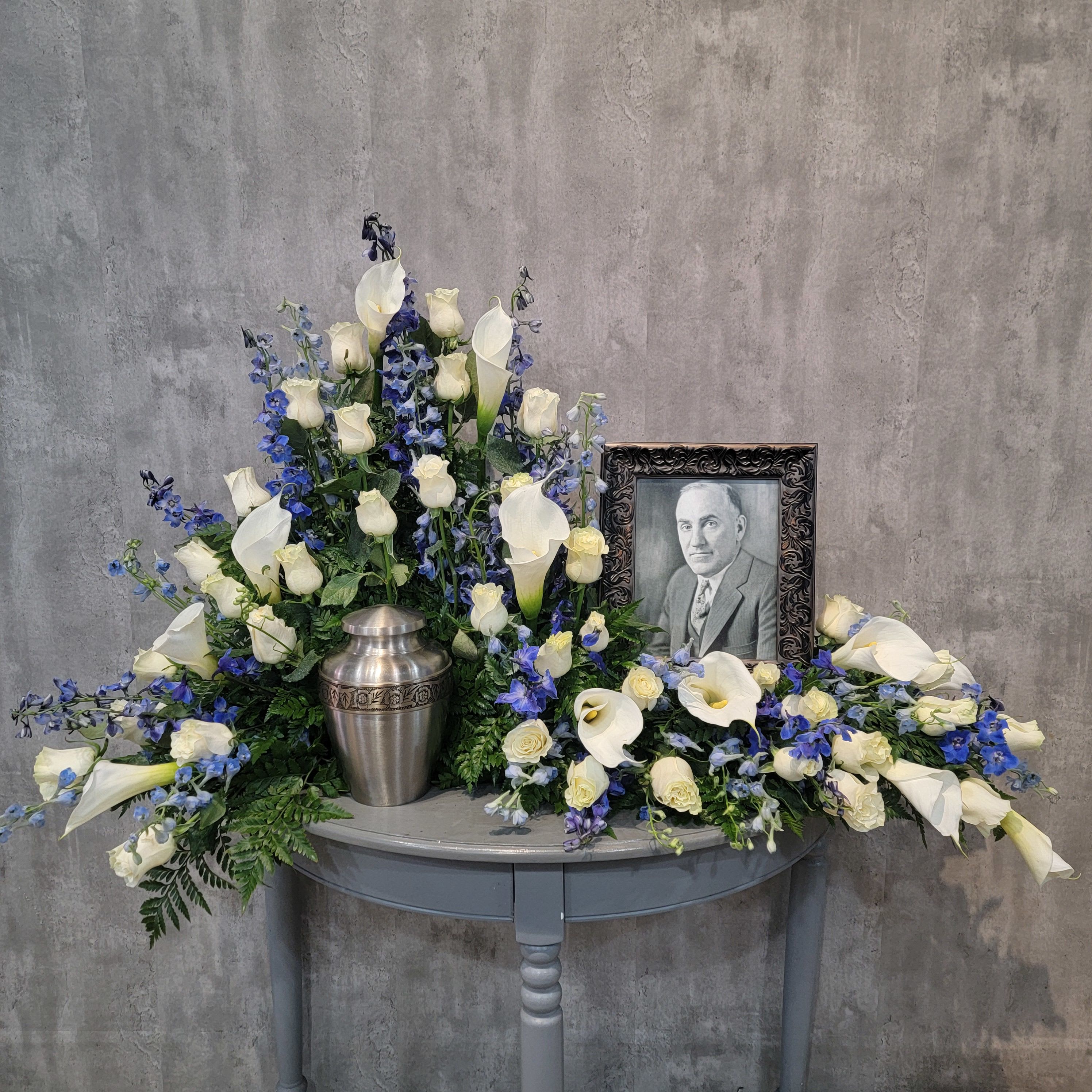 White calla lilies and roses arranged around a framed portrait and urn.
