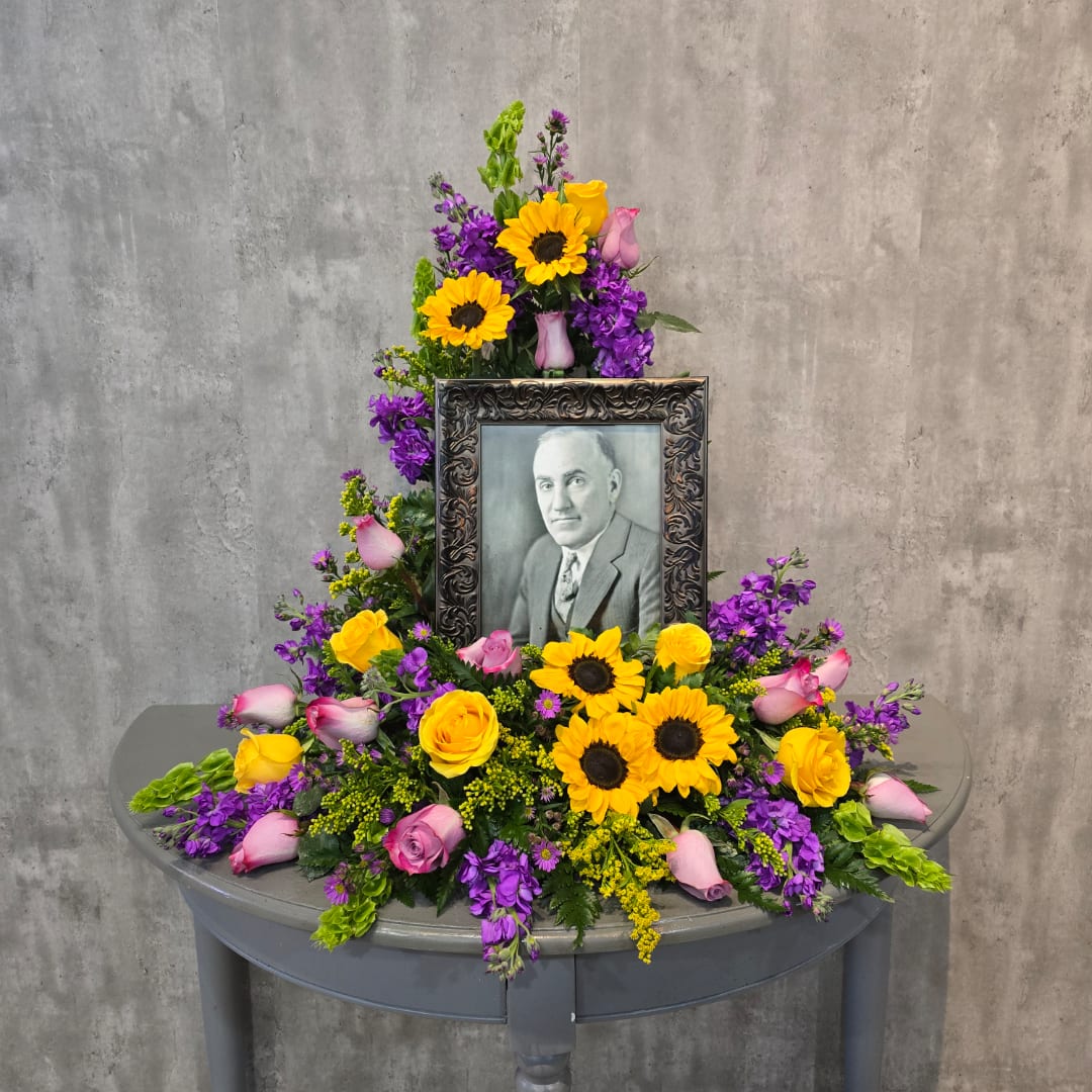 Floral tribute around a framed black-and-white portrait with yellow sunflowers and pink roses