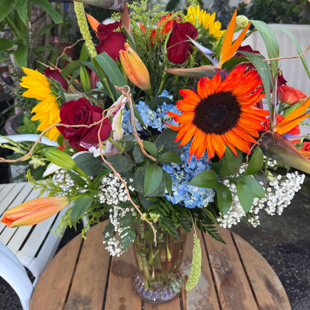 Colorful mixed bouquet in a clear glass vase with sunflowers, roses, and lilies