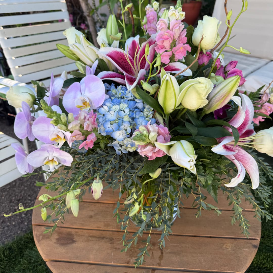 Mixed bouquet with lilies, orchids, hydrangea, and pink blooms in a glass vase