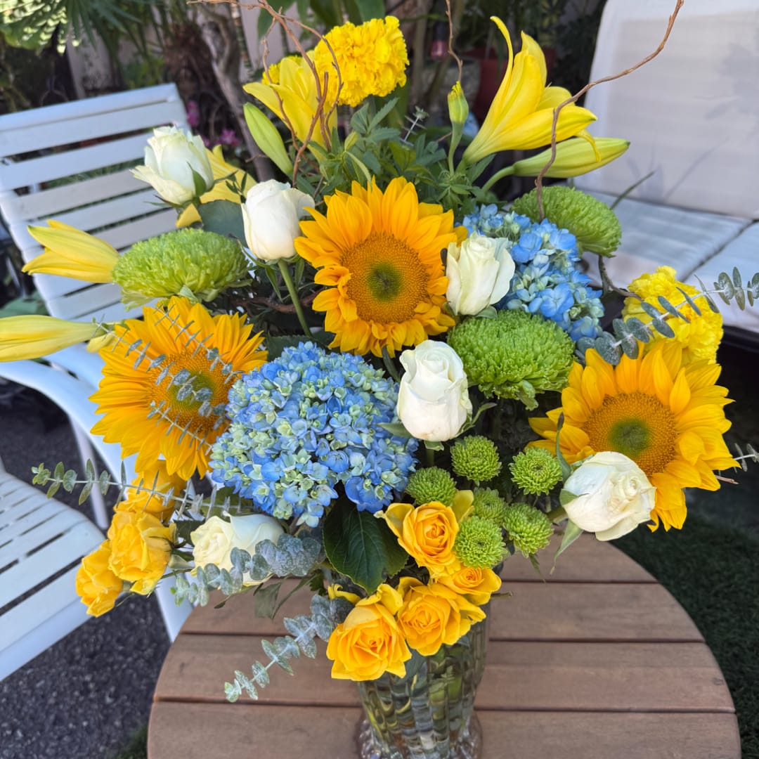 Bouquet of sunflowers, white roses, blue hydrangeas, and yellow lilies in a glass vase