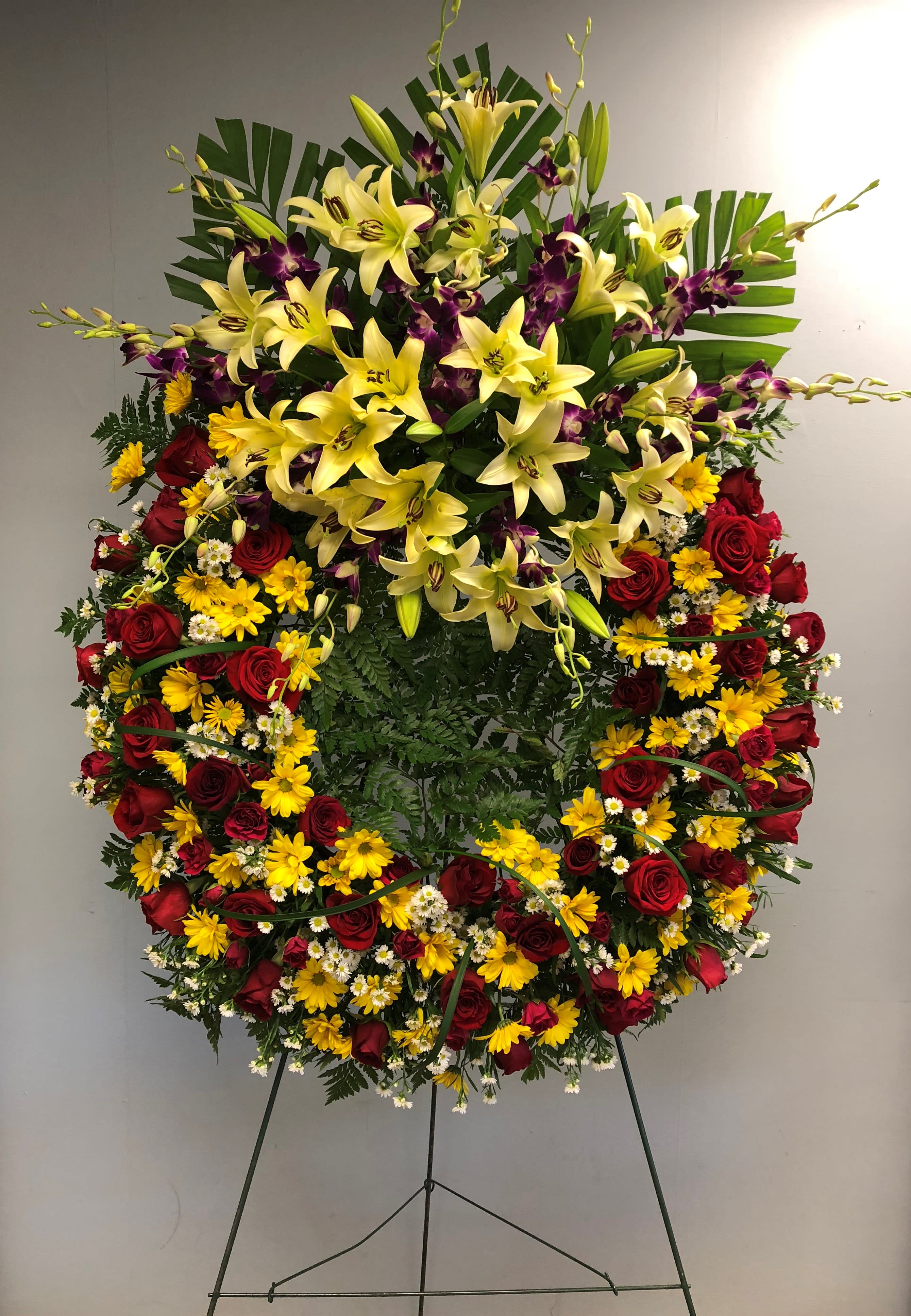 Large standing floral spray with yellow lilies, red roses, and purple orchids