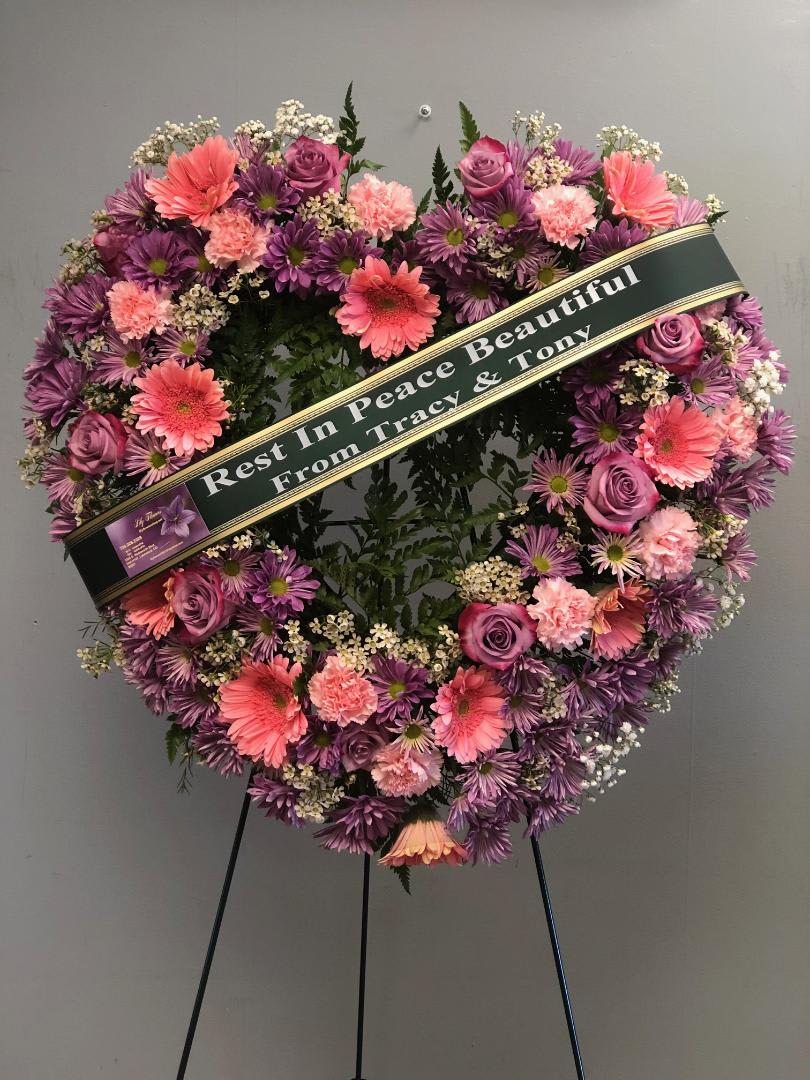 Heart-shaped funeral wreath with pink and purple flowers on a stand