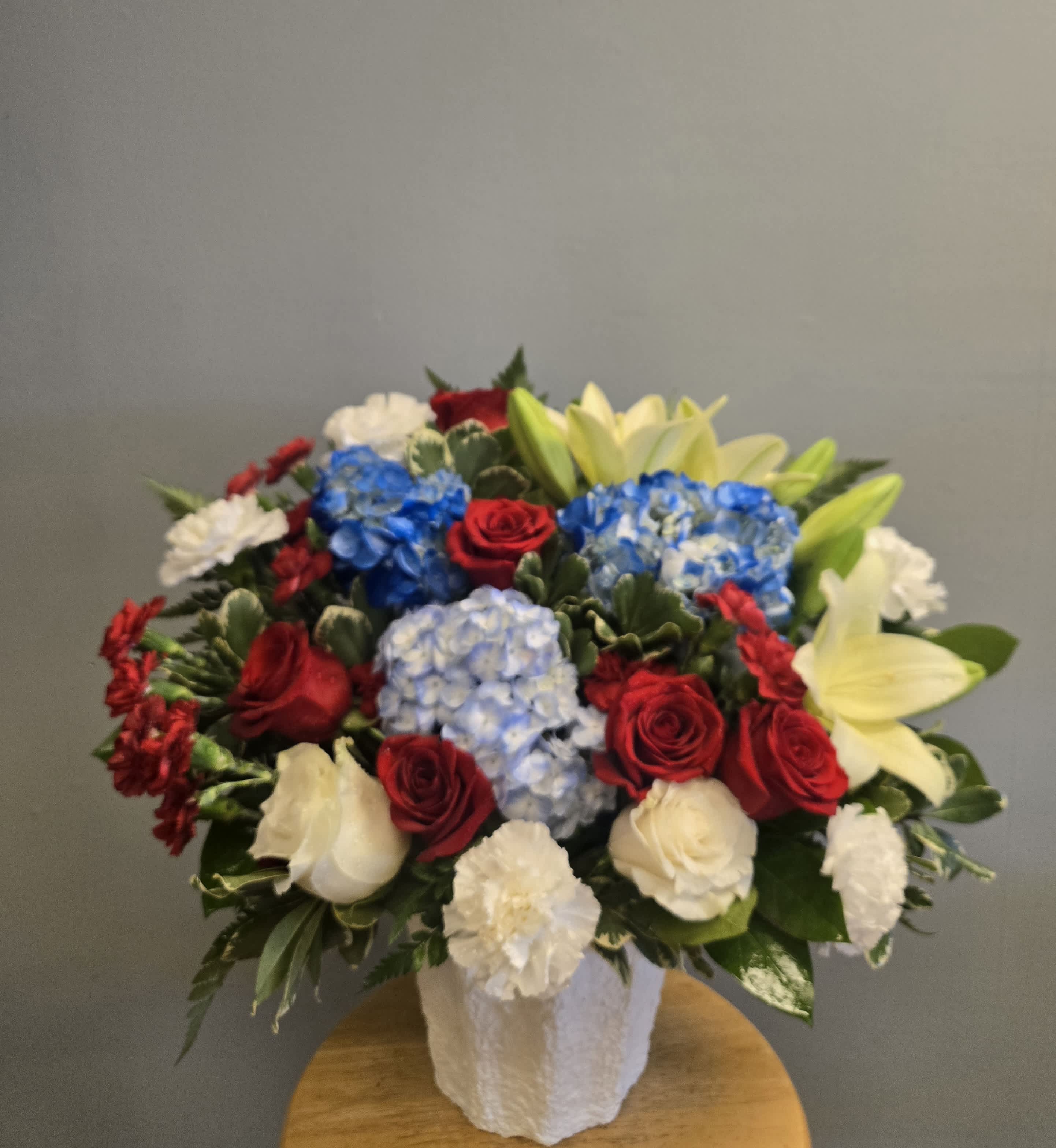 Mixed bouquet of red roses, blue hydrangeas, white carnations, and pale lilies in a white vase