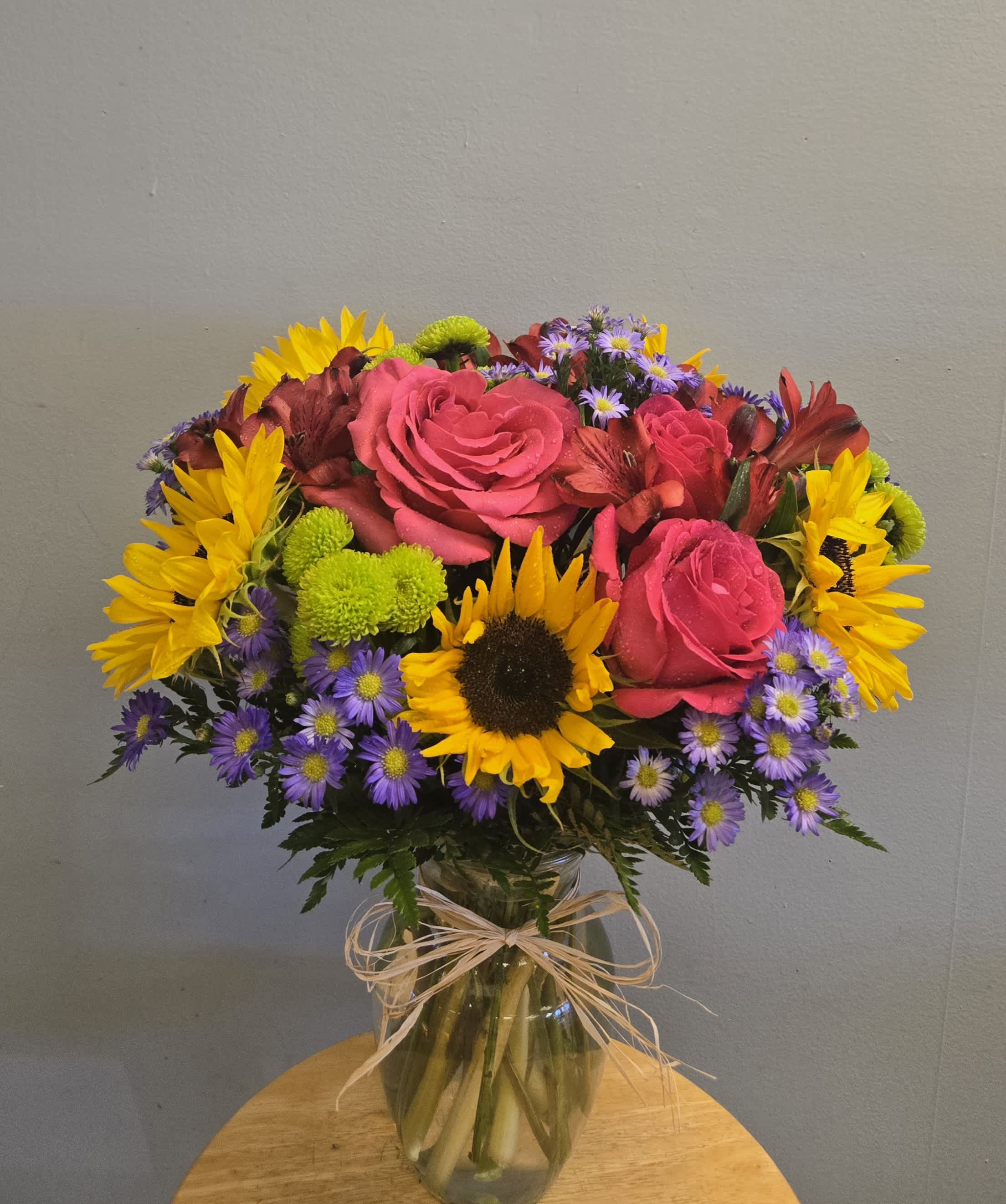 Bouquet of pink roses, sunflowers, and purple daisies in a glass vase