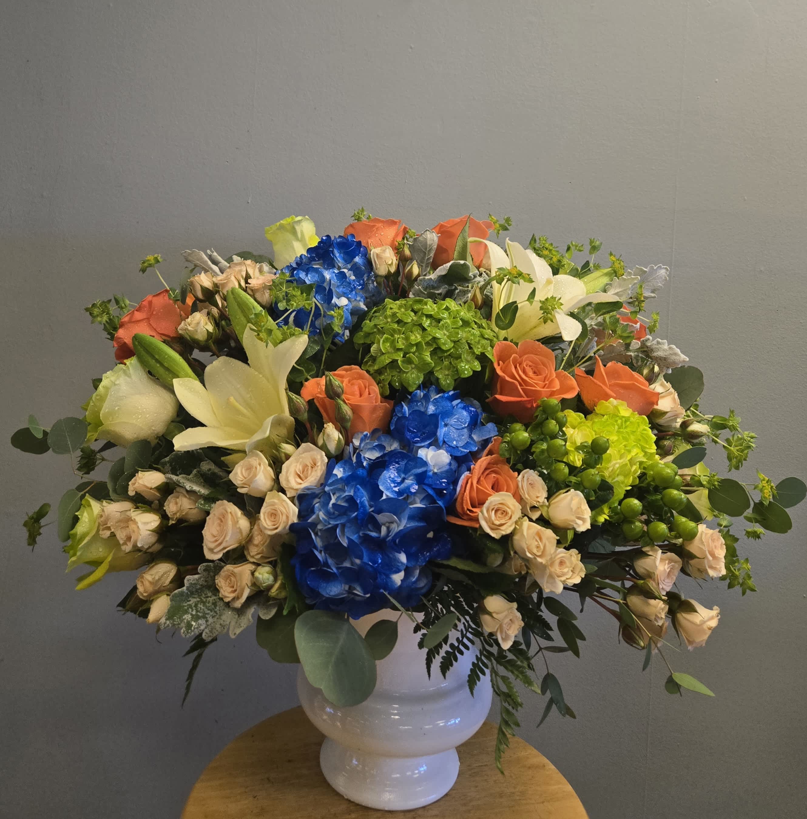 Large mixed bouquet in a white vase with blue, orange, cream, and green blooms