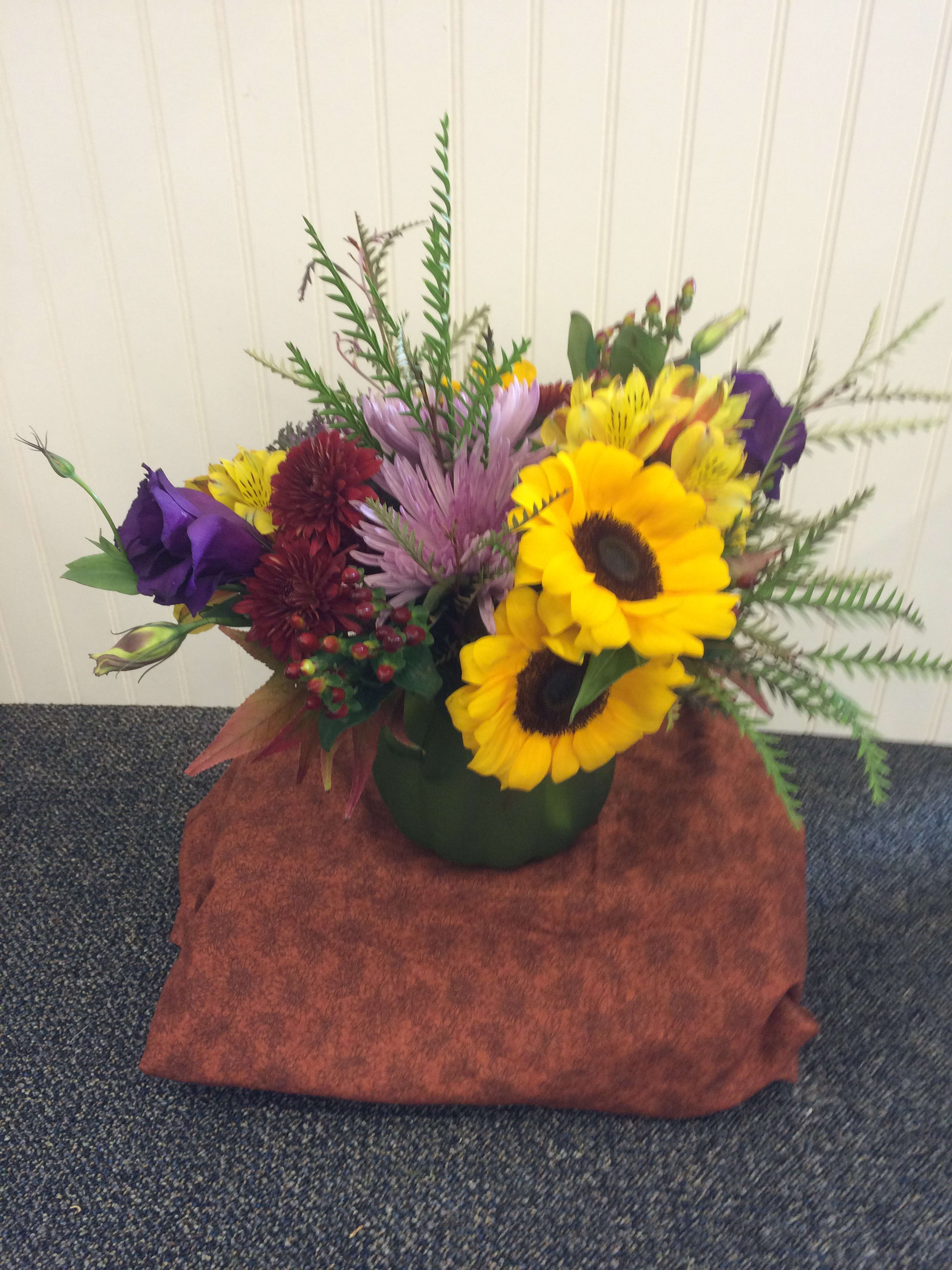 Mixed bouquet with sunflowers, purple blooms, and red flowers in a green vase