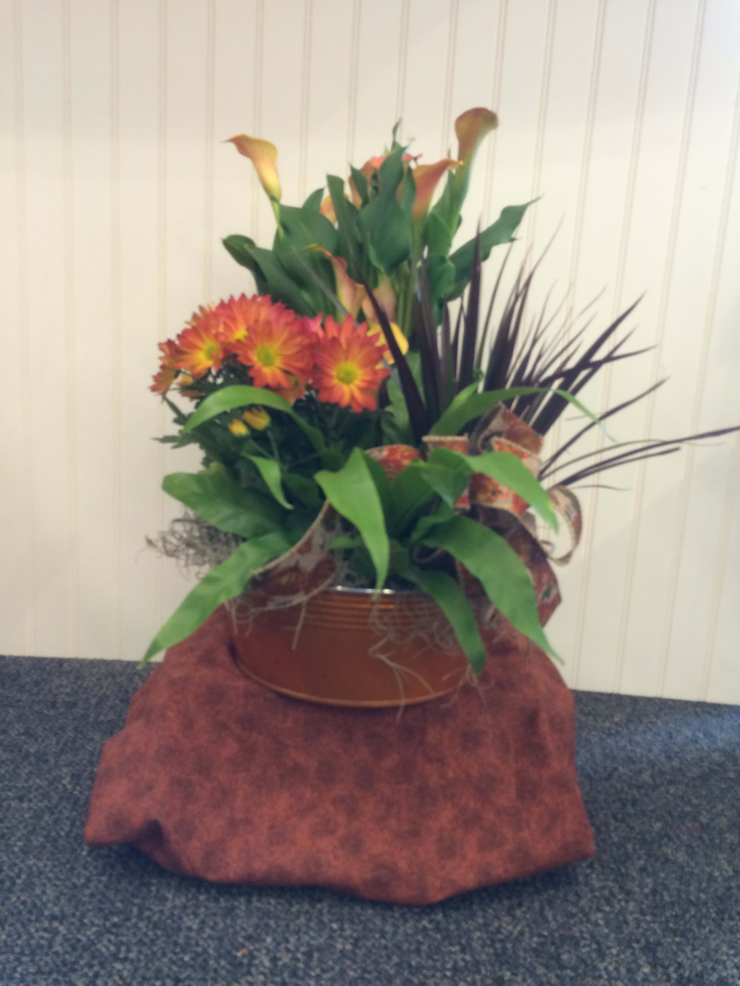 Orange chrysanthemums and calla lilies in a copper-toned container