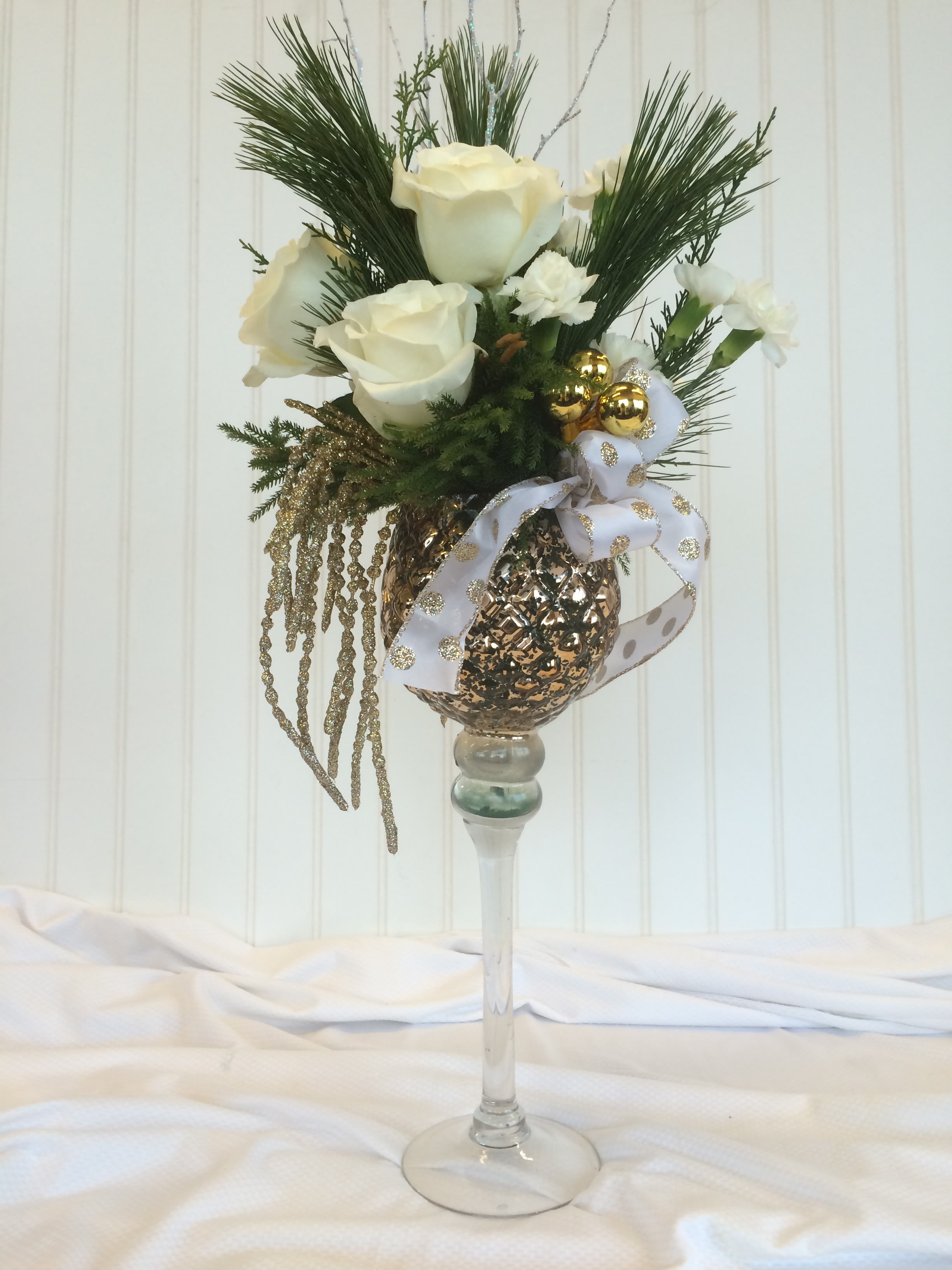 White roses arranged in a tall glass vase with gold ornaments and ribbon