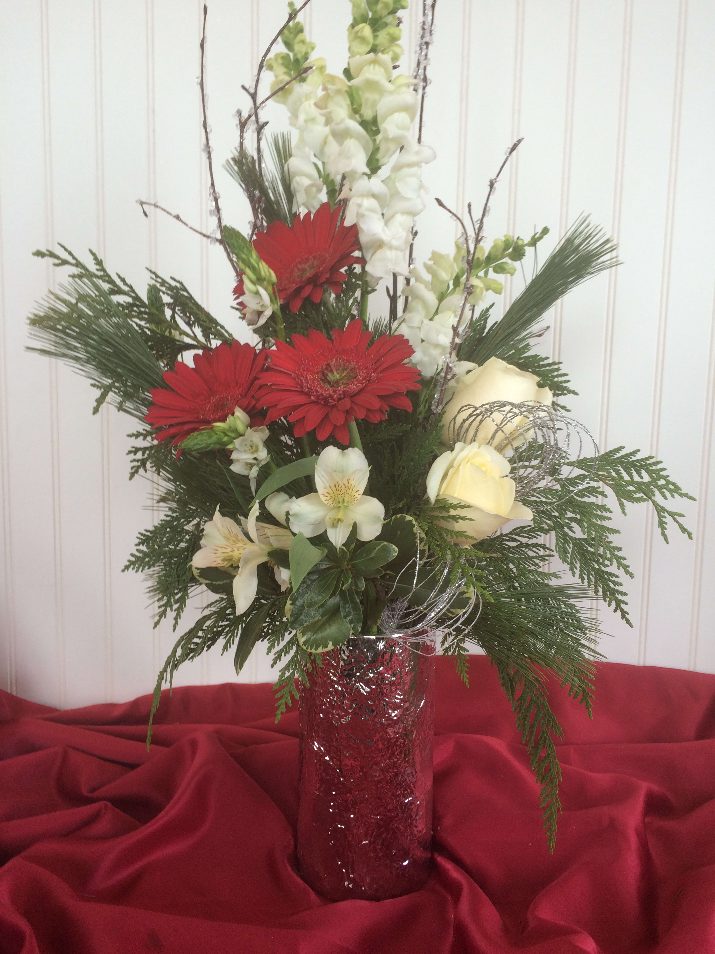 Tall floral arrangement with red gerbera daisies, white blooms, and a red vase