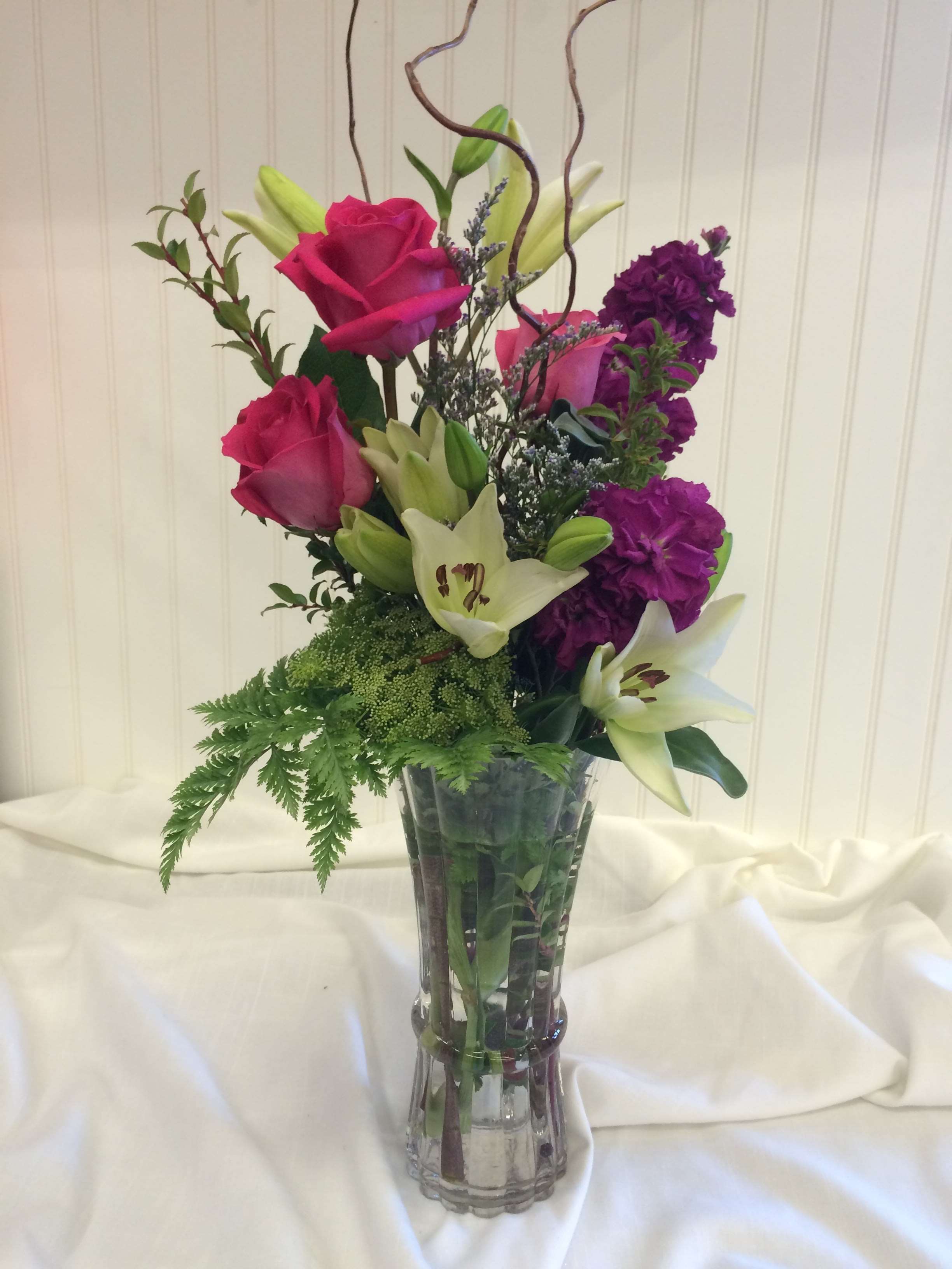 Tall bouquet of pink roses, white lilies, and purple flowers in a glass vase