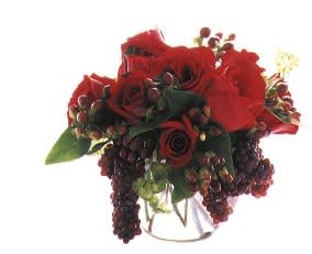 Red rose bouquet with dark berry accents in a clear vase