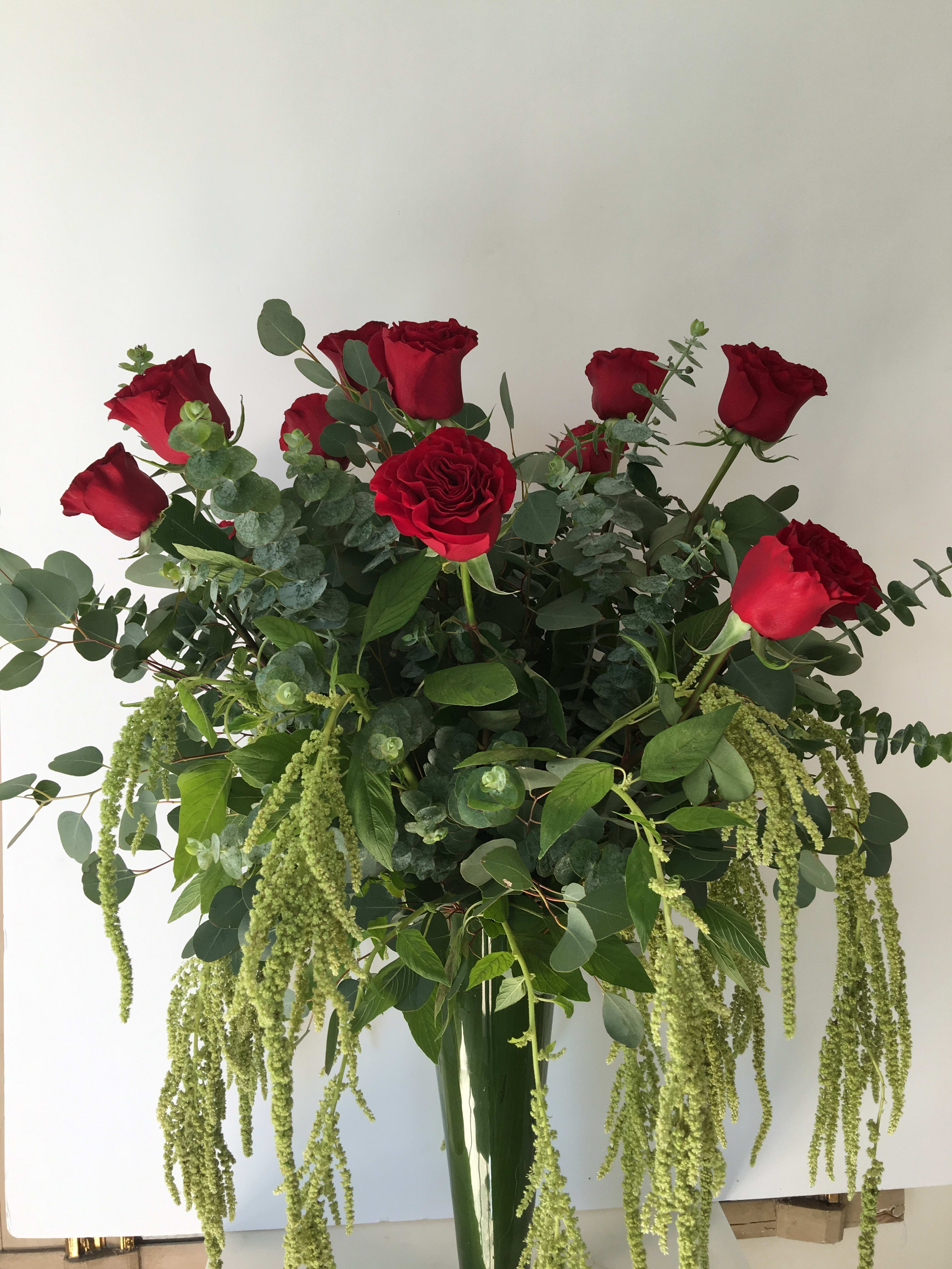 Tall bouquet of red roses with cascading green foliage in a glass vase