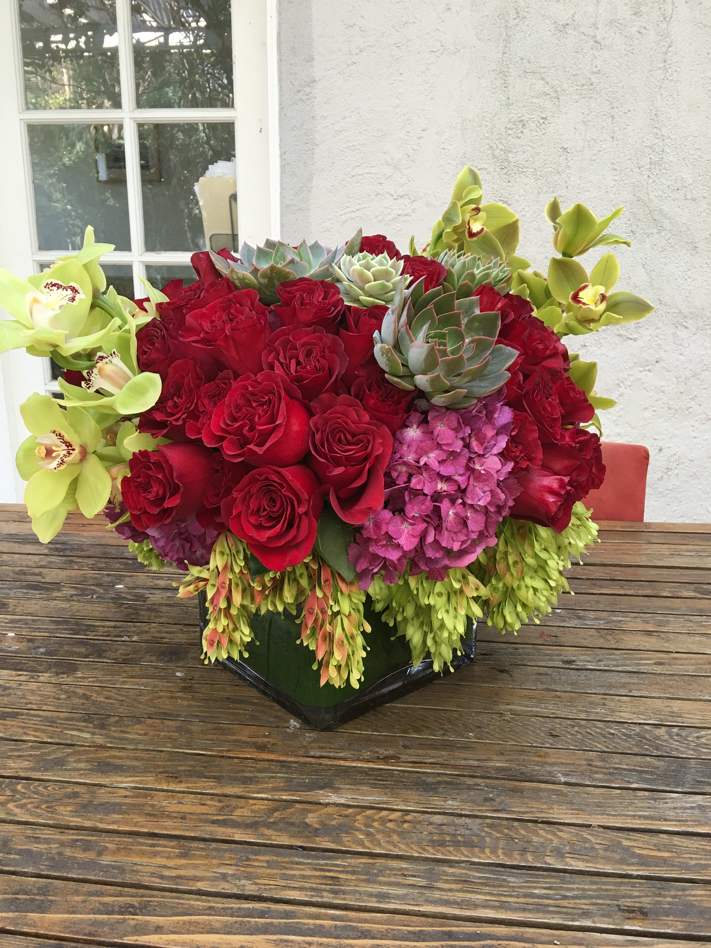 Red roses with green orchids and succulents in a black vase