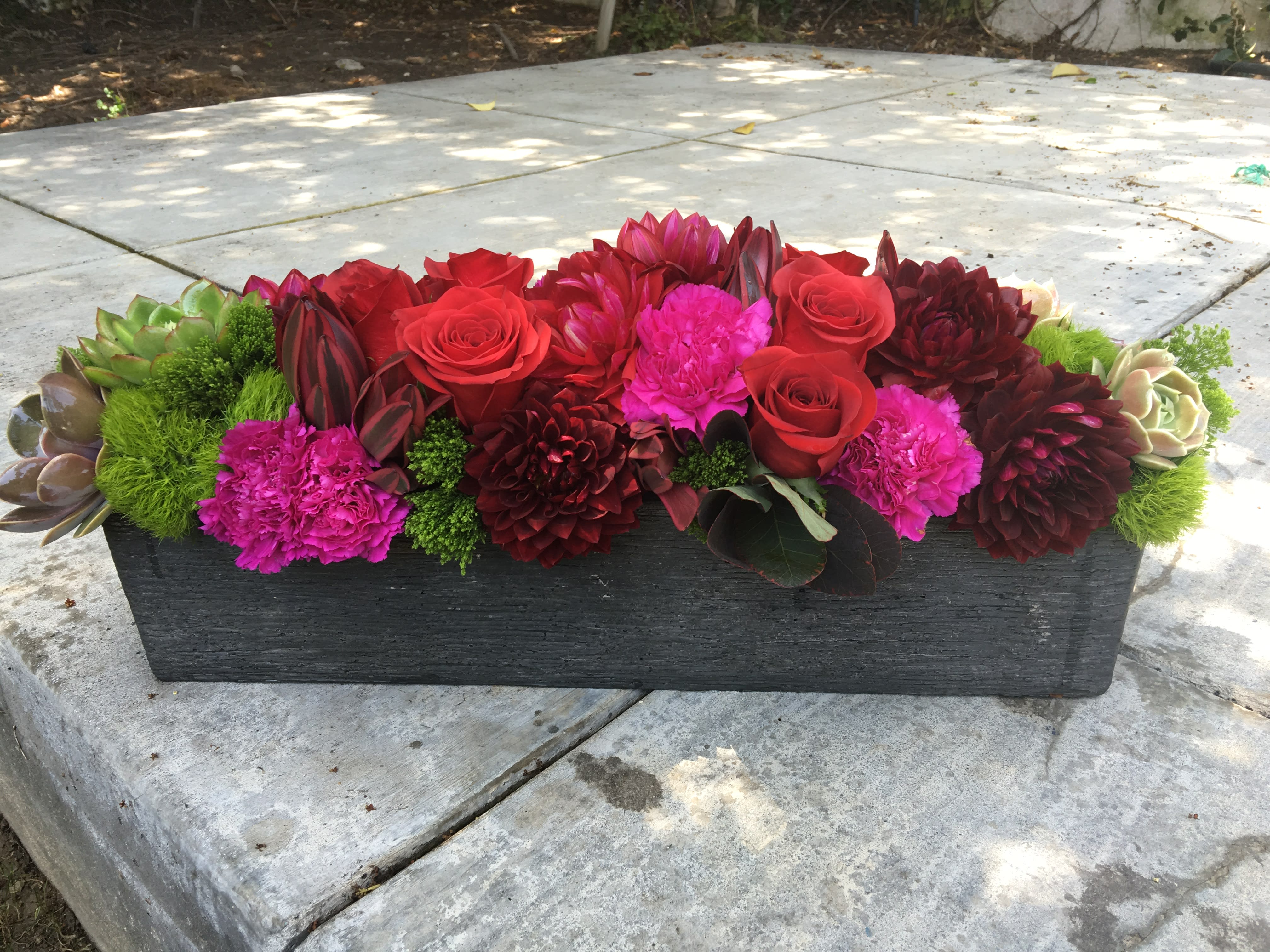 Low rectangular arrangement of red and pink flowers in a dark planter