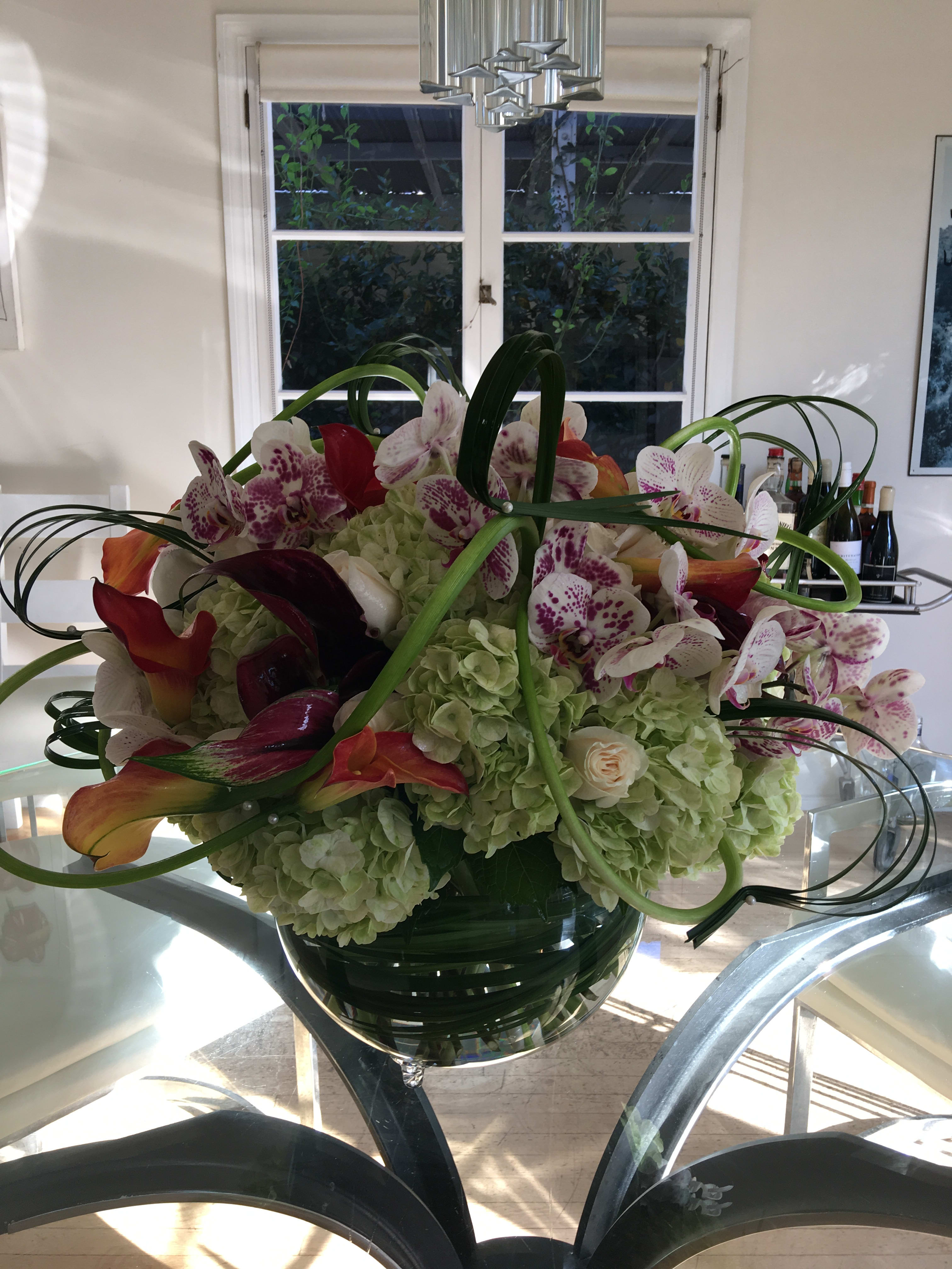 Large floral arrangement with orchids, hydrangeas, and calla lilies in a glass vase