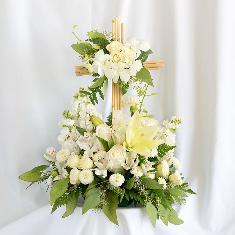 White floral arrangement on a wooden cross with lilies and roses