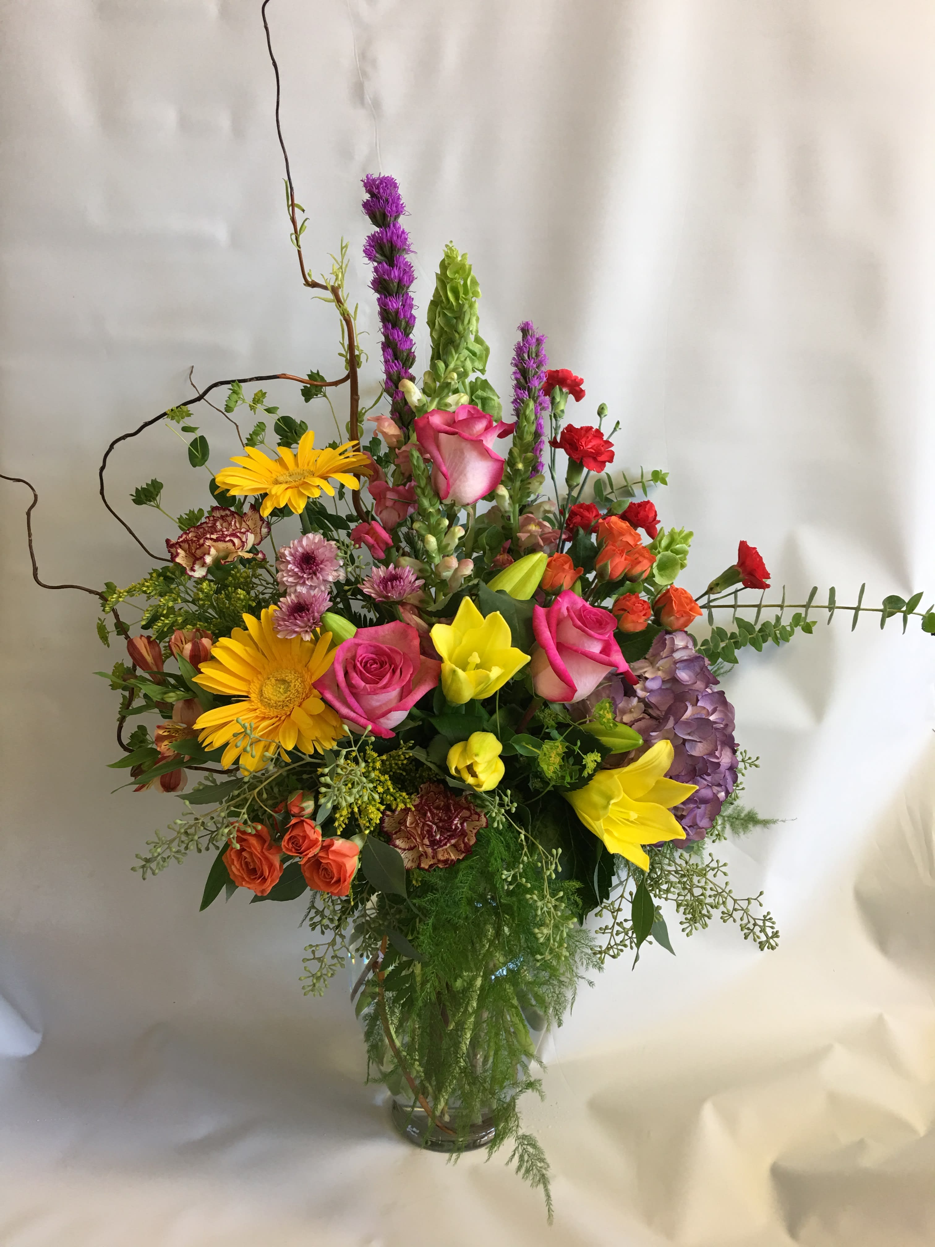 Colorful mixed bouquet in a clear glass vase with roses, lilies, and gerbera daisies