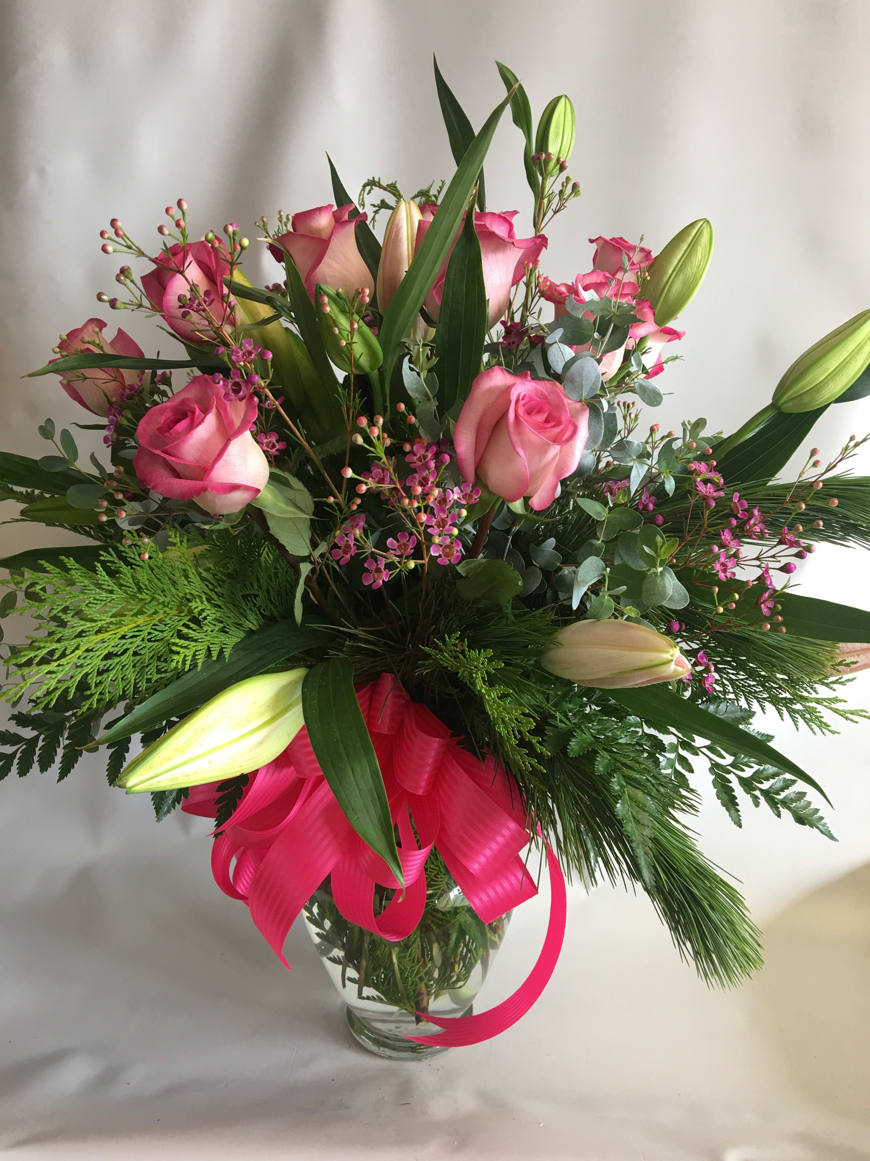 Pink roses and lilies in a glass vase with a bright ribbon