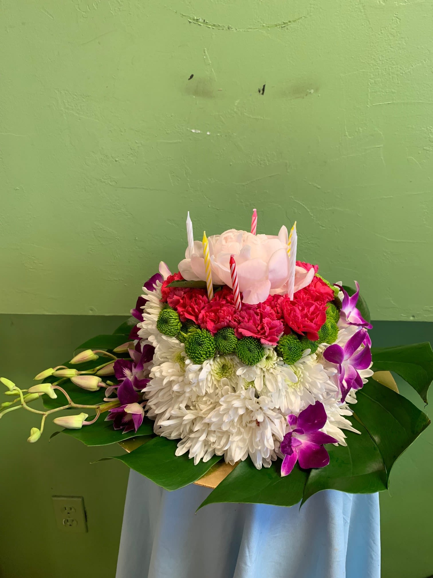 Round floral cake with candles, white chrysanthemums, pink blooms, and purple orchids