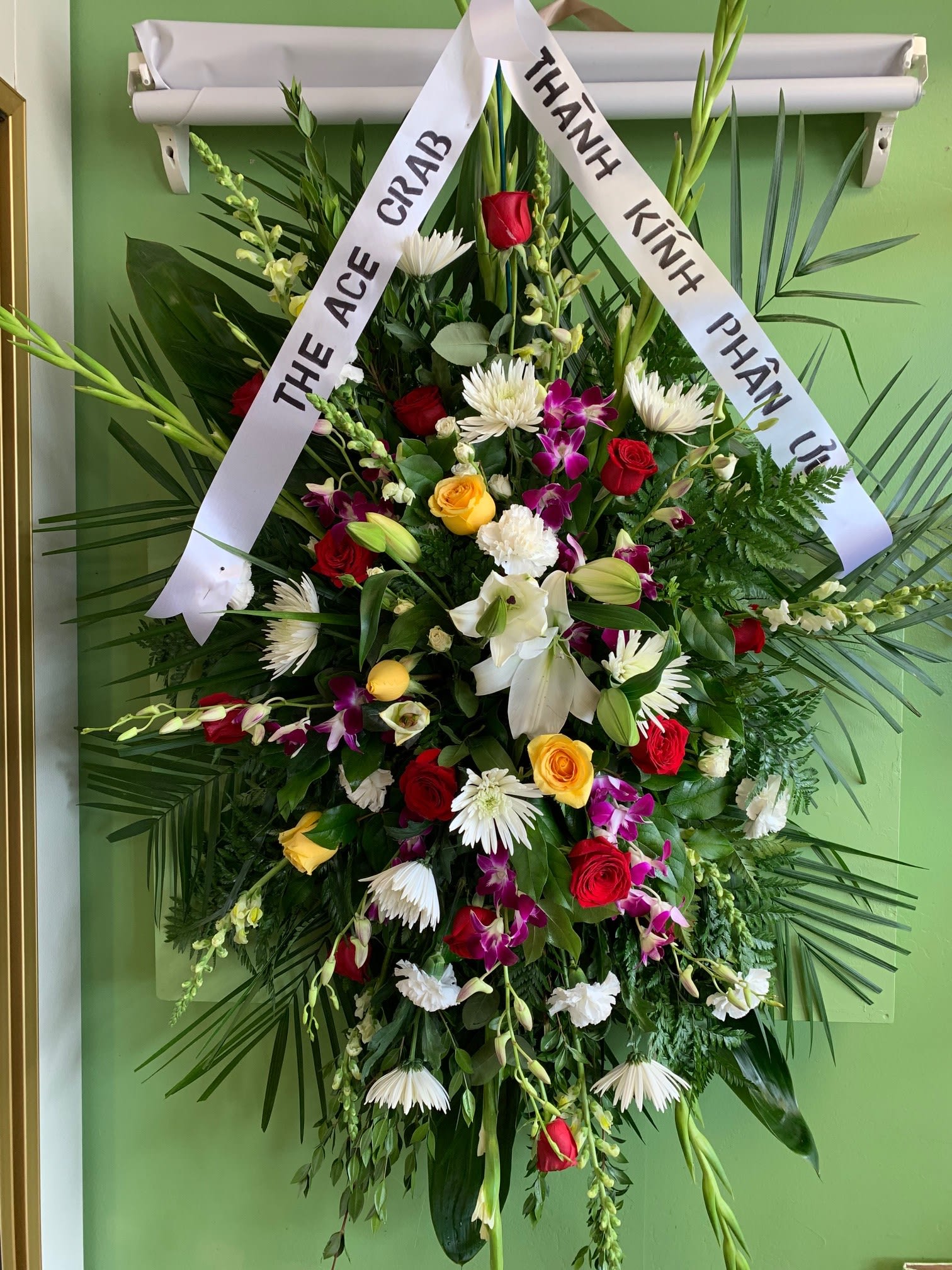 Large funeral wreath with mixed flowers and white condolence ribbons