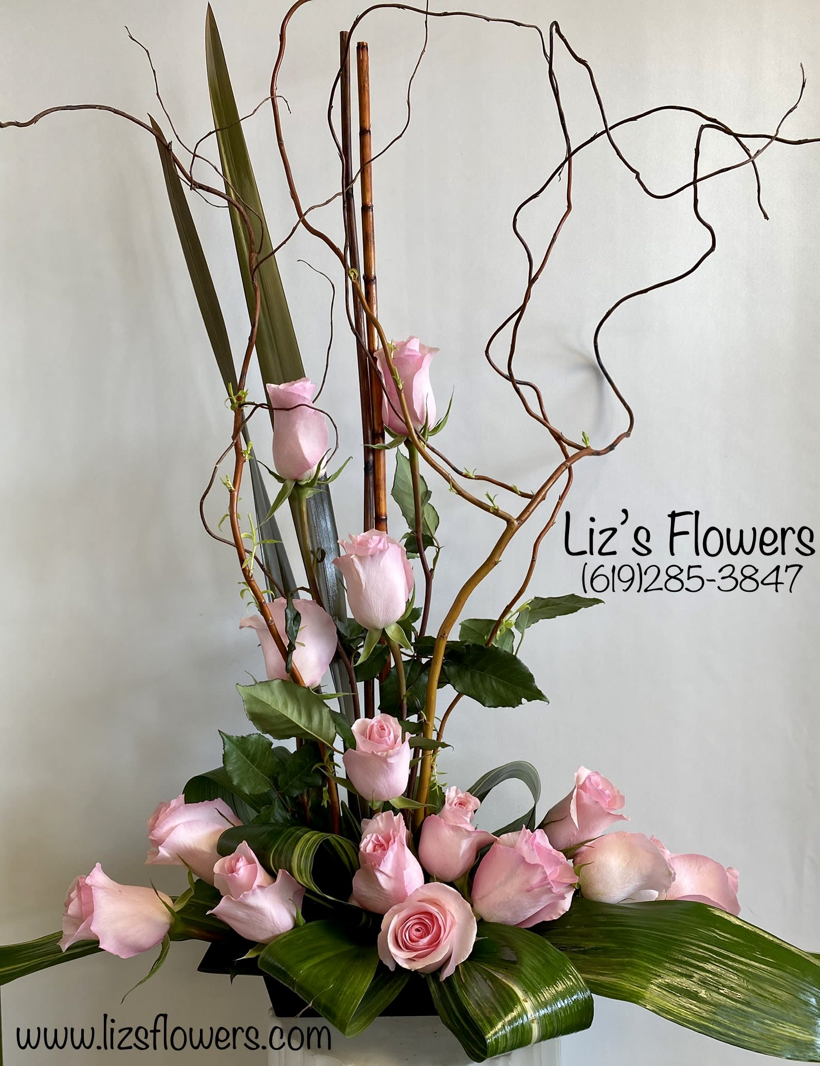 Tall arrangement of pink roses with curly branches and broad leaves