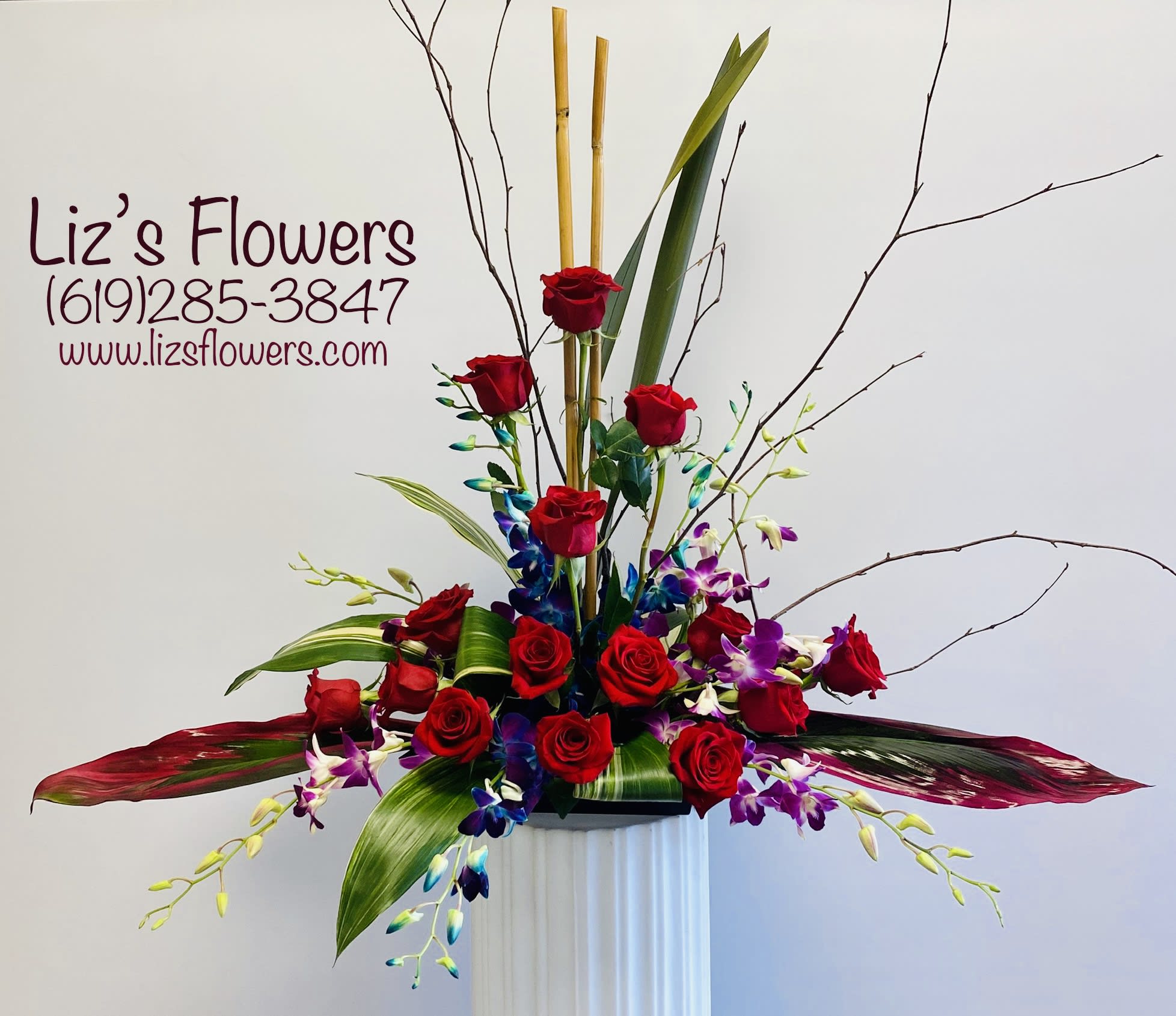 Tall arrangement of red roses and purple orchids in a white pedestal vase