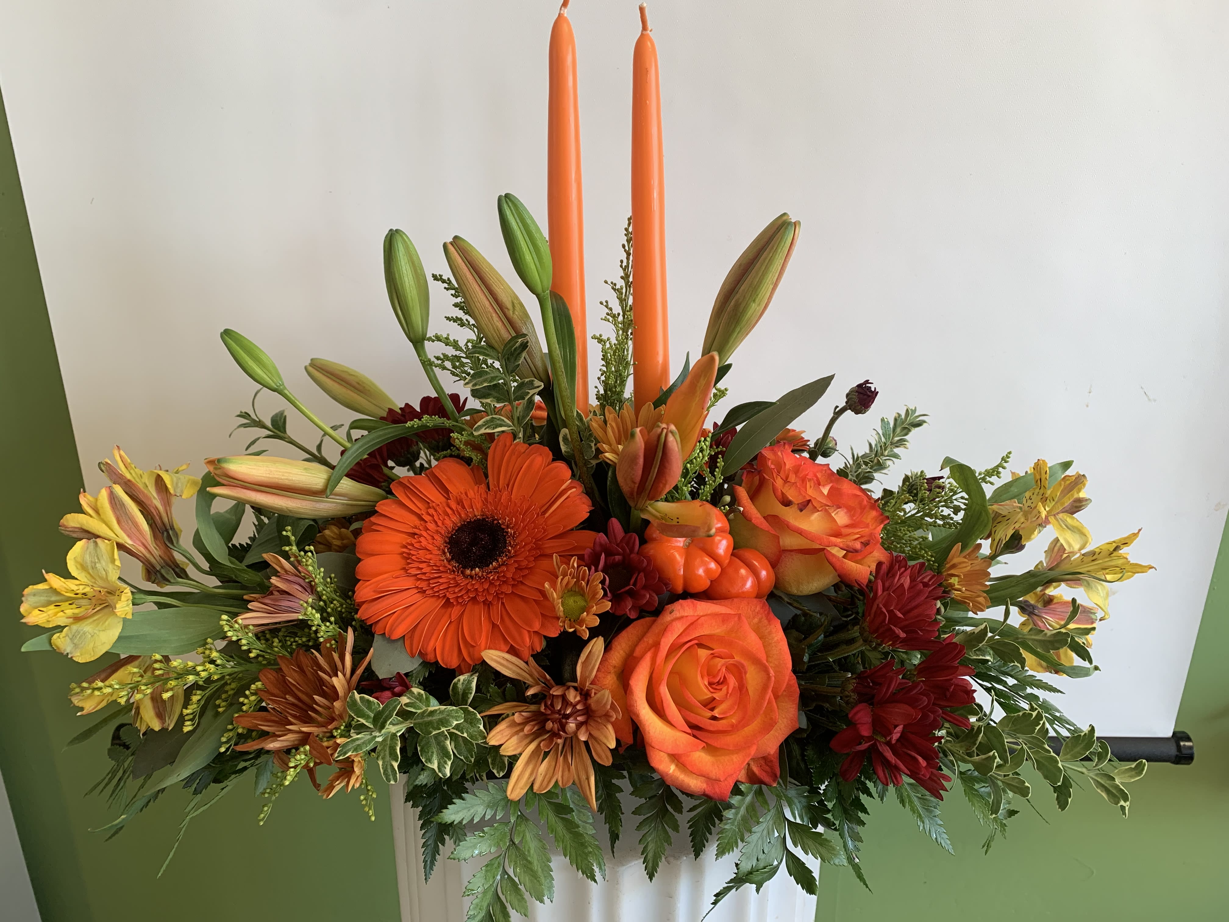 Orange and yellow floral arrangement with two tall orange candles