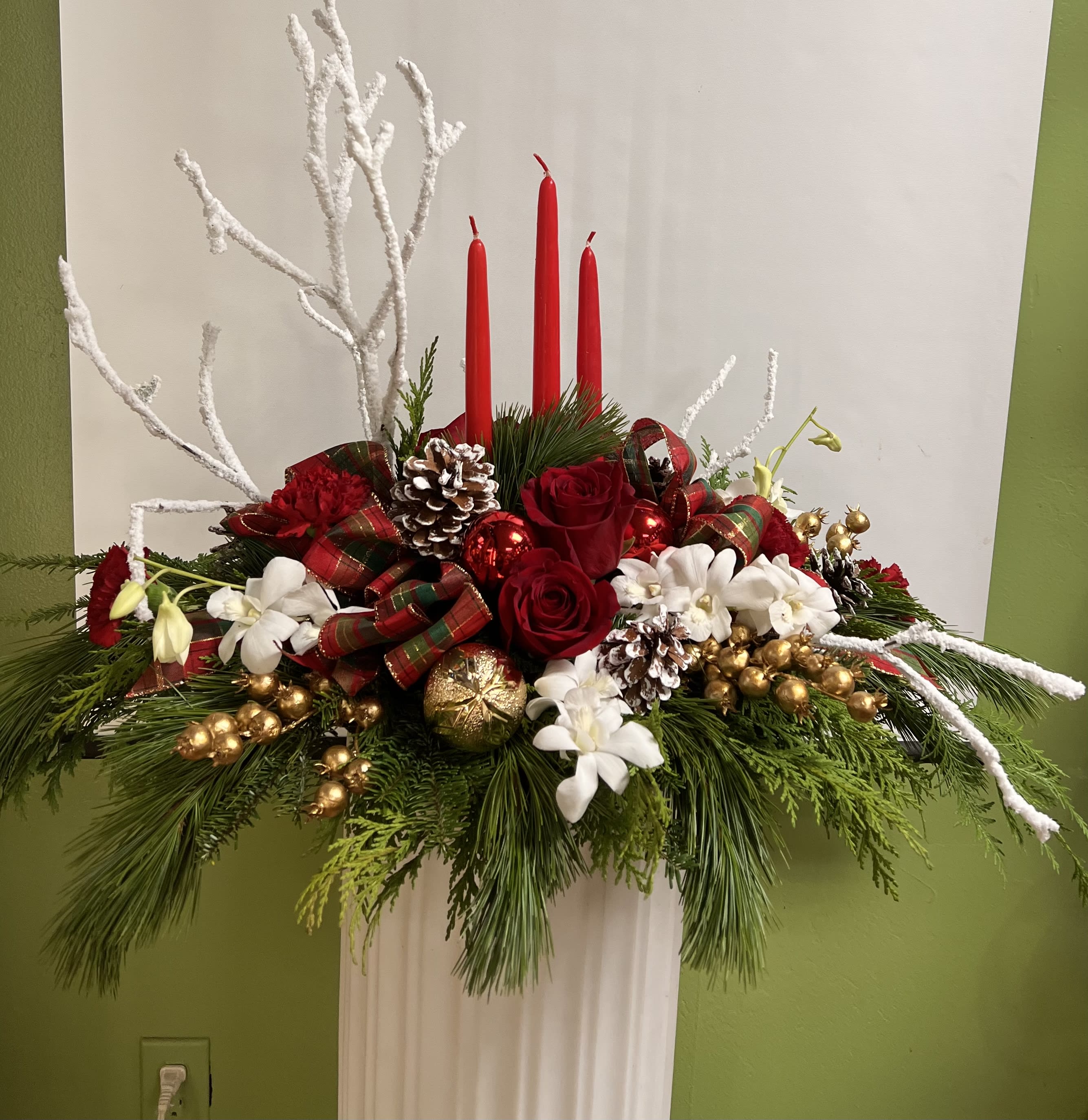 Holiday centerpiece with red roses, white flowers, and red candles in a white pedestal vase