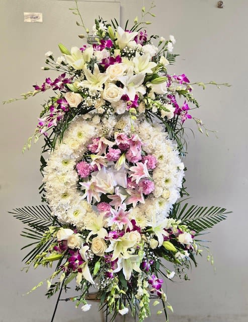 Large standing floral wreath with white lilies, roses, and pink orchids