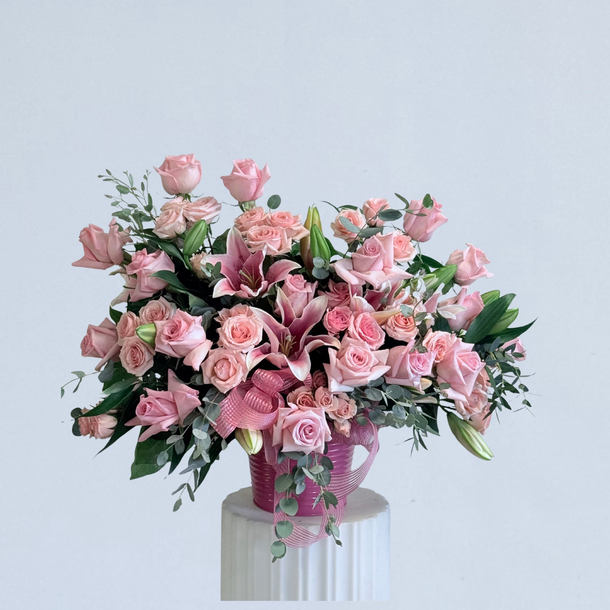 Pink roses and lilies arranged in a pink vase with ribbon