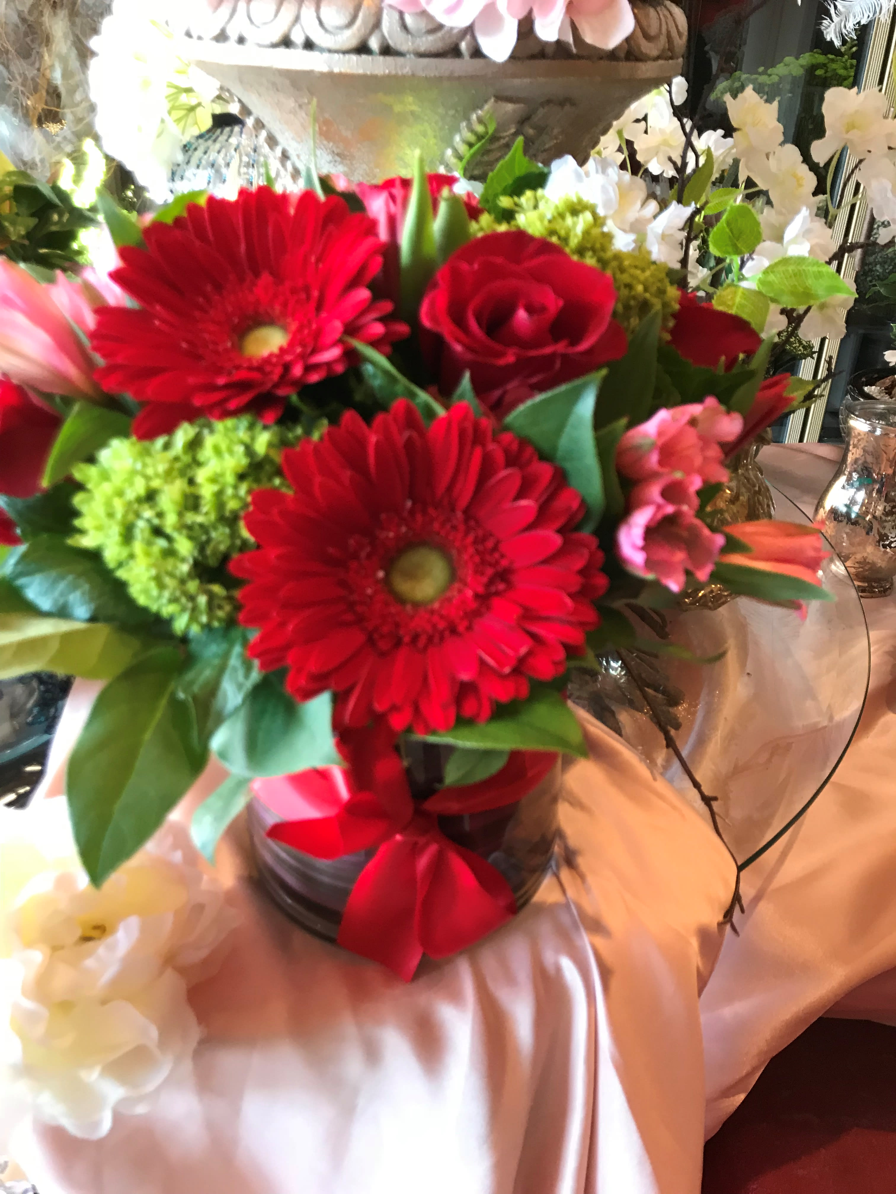 Bouquet of red gerbera daisies and roses in a glass vase with a red ribbon