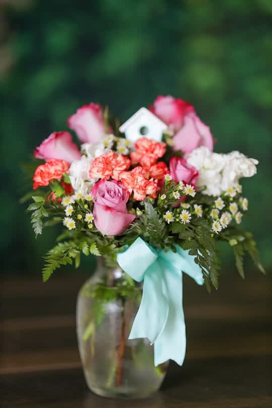 Pink roses and carnations in a glass vase with a blue ribbon