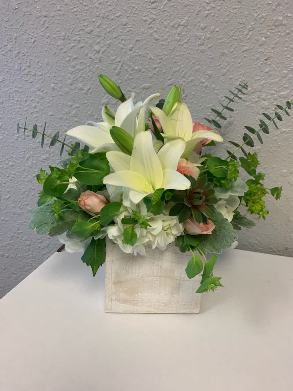 White lilies and pale pink roses arranged in a square vase