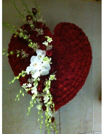 Heart-shaped red floral arrangement with white orchids and trailing greenery