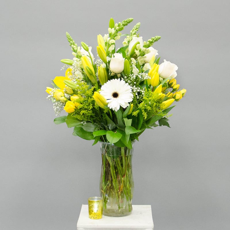 Yellow and white bouquet in a glass vase with a small candle